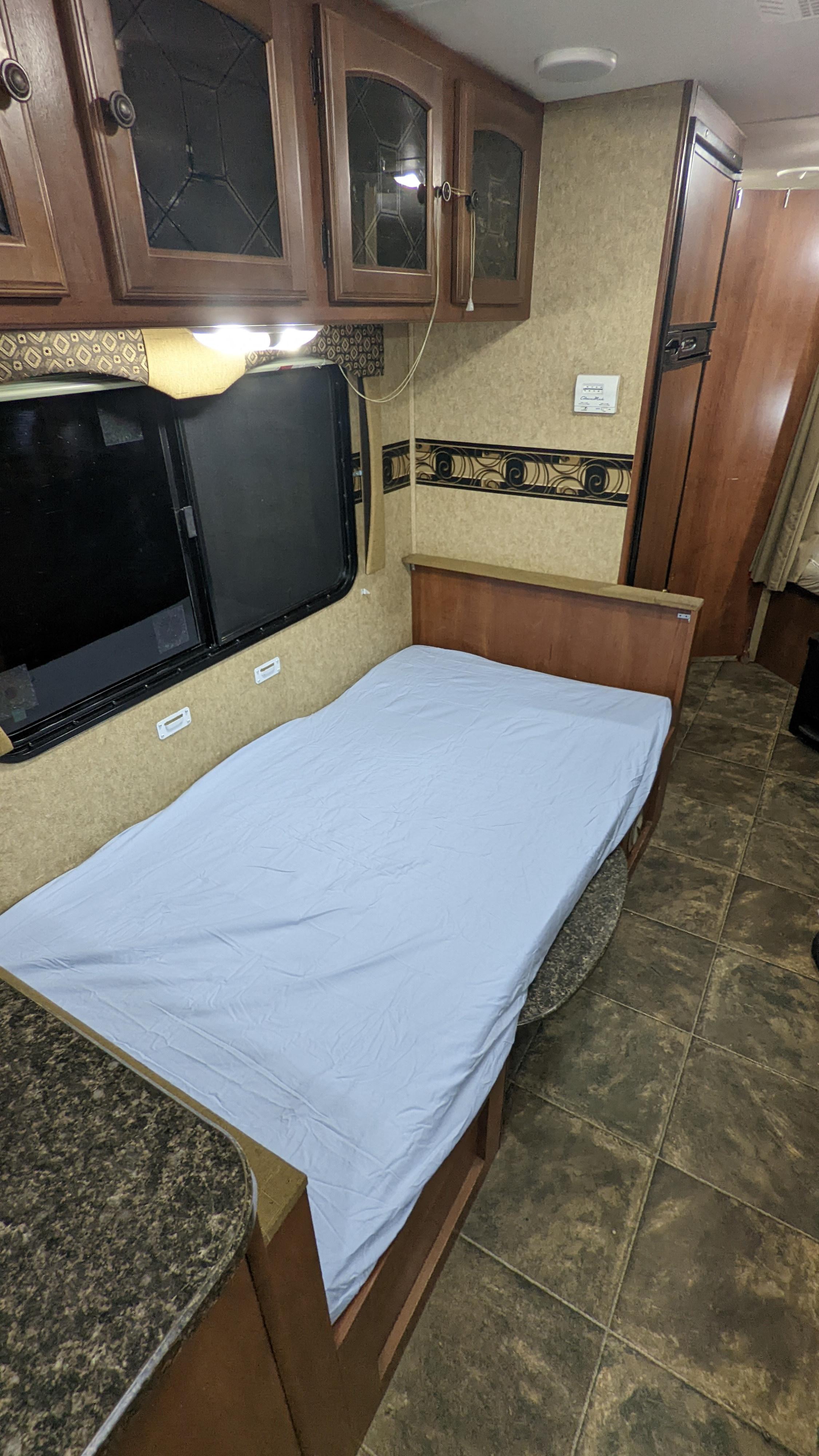 RV rental interior. This bedroom has a bed with light blue sheet, wooden cabinets above, a window, and tiled floor.. Heartland RVs North Trail 2013