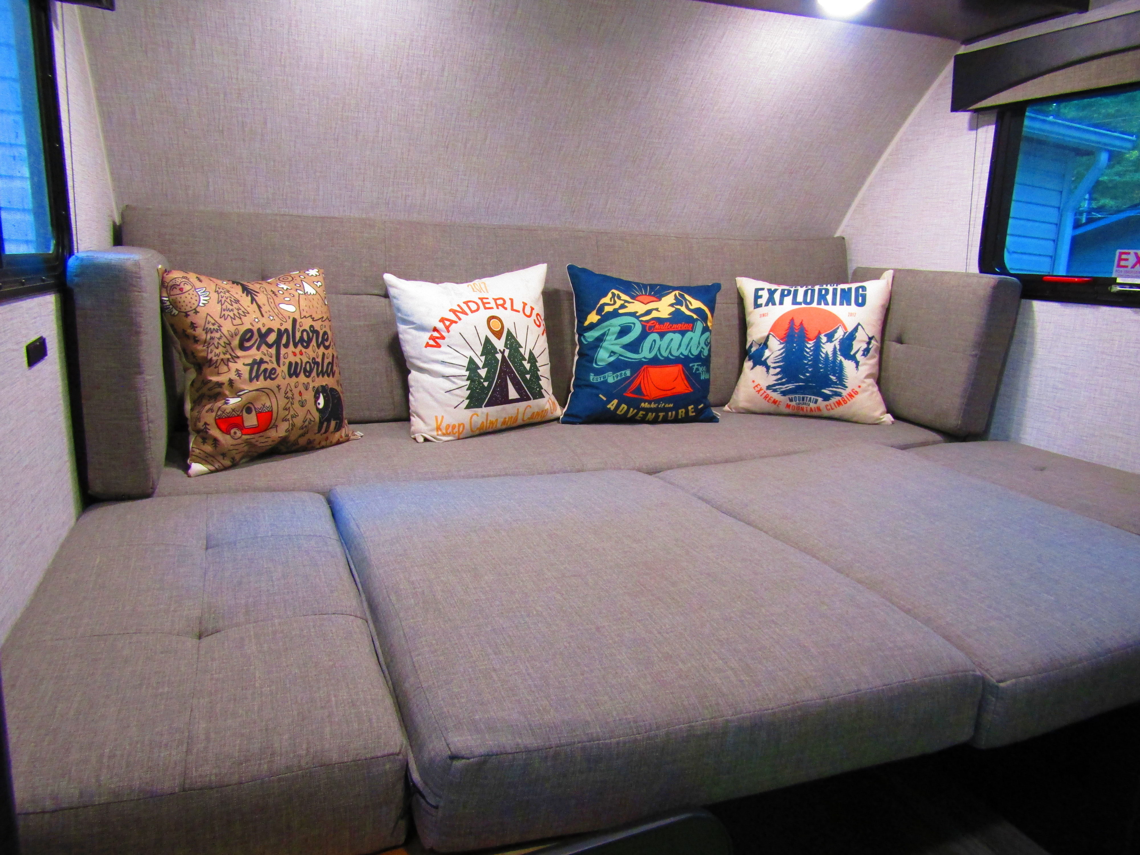 RV rental interior: A cozy gray sofa with four adventure-themed pillows, ideal for travel comfort and camping trips.. Braxton Creek Bushwhacker Plus 2021