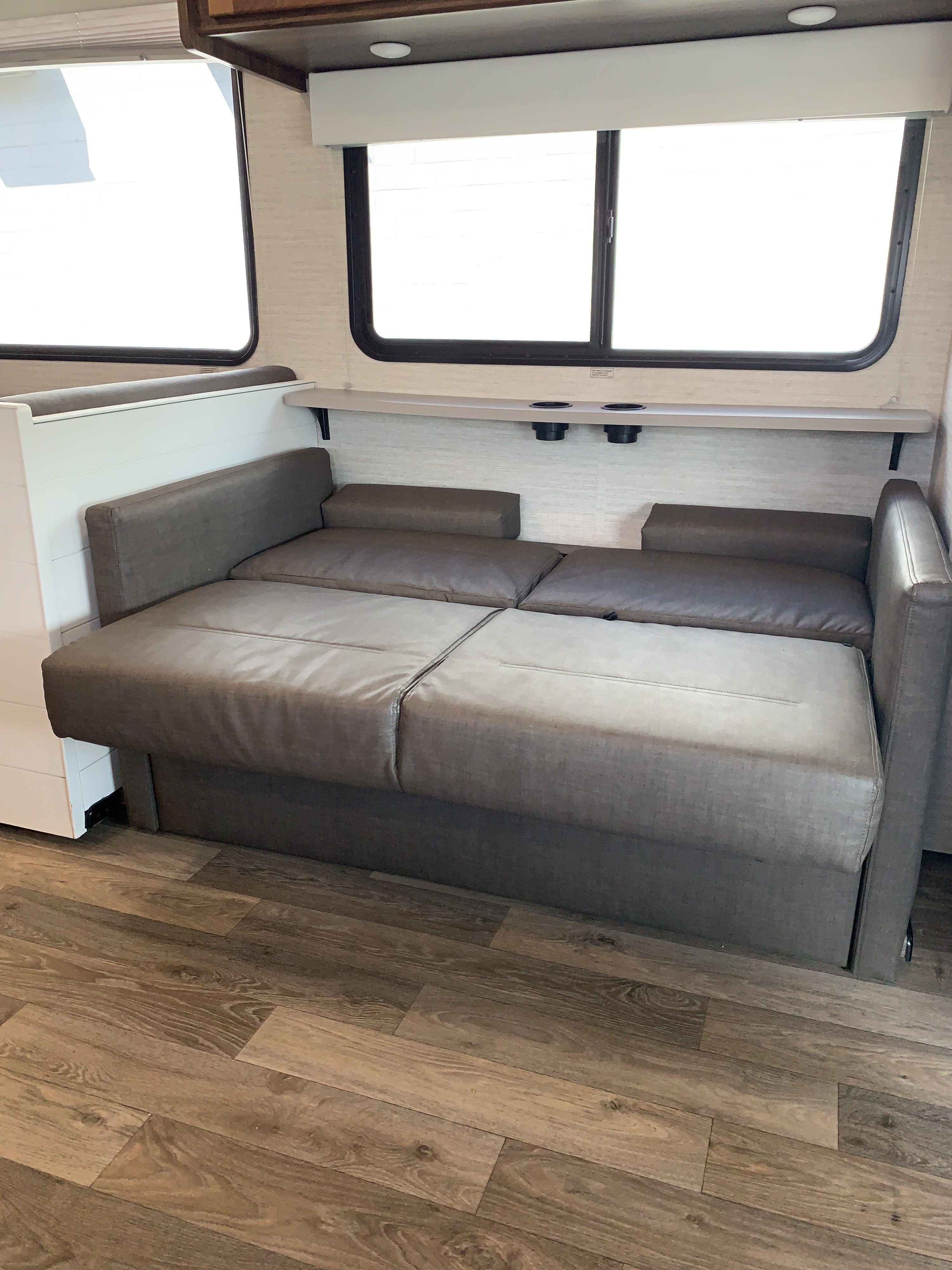 Comfortable RV rental interior featuring a convertible sofa bed, large windows, and cup holders on a shelf.. Winnebago Outlook 2020