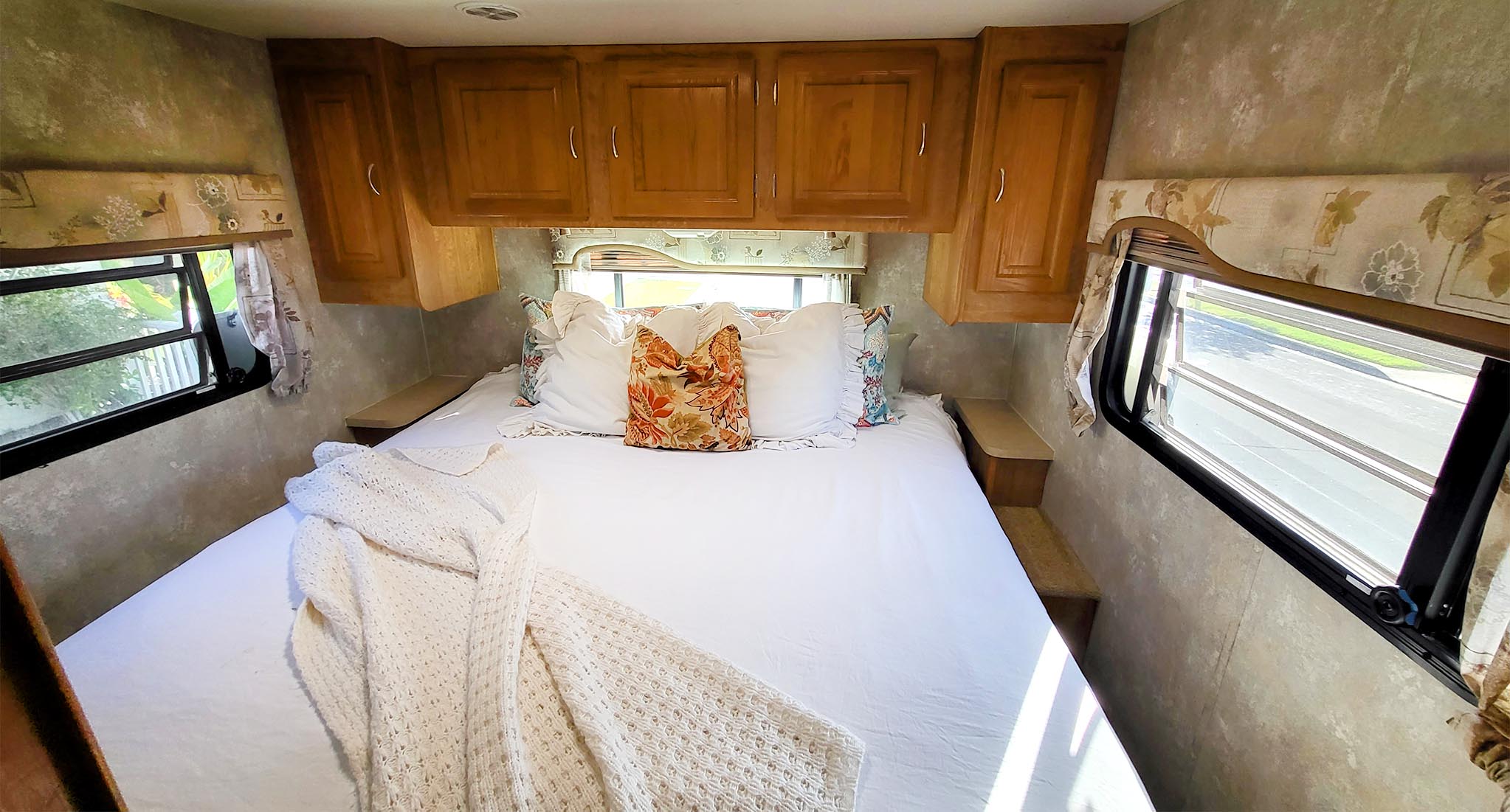 An inviting RV rental bedroom interior with a spacious bed, crisp white bedding, overhead wood cabinets, and two windows.. Georgie Boy Maverick 2005