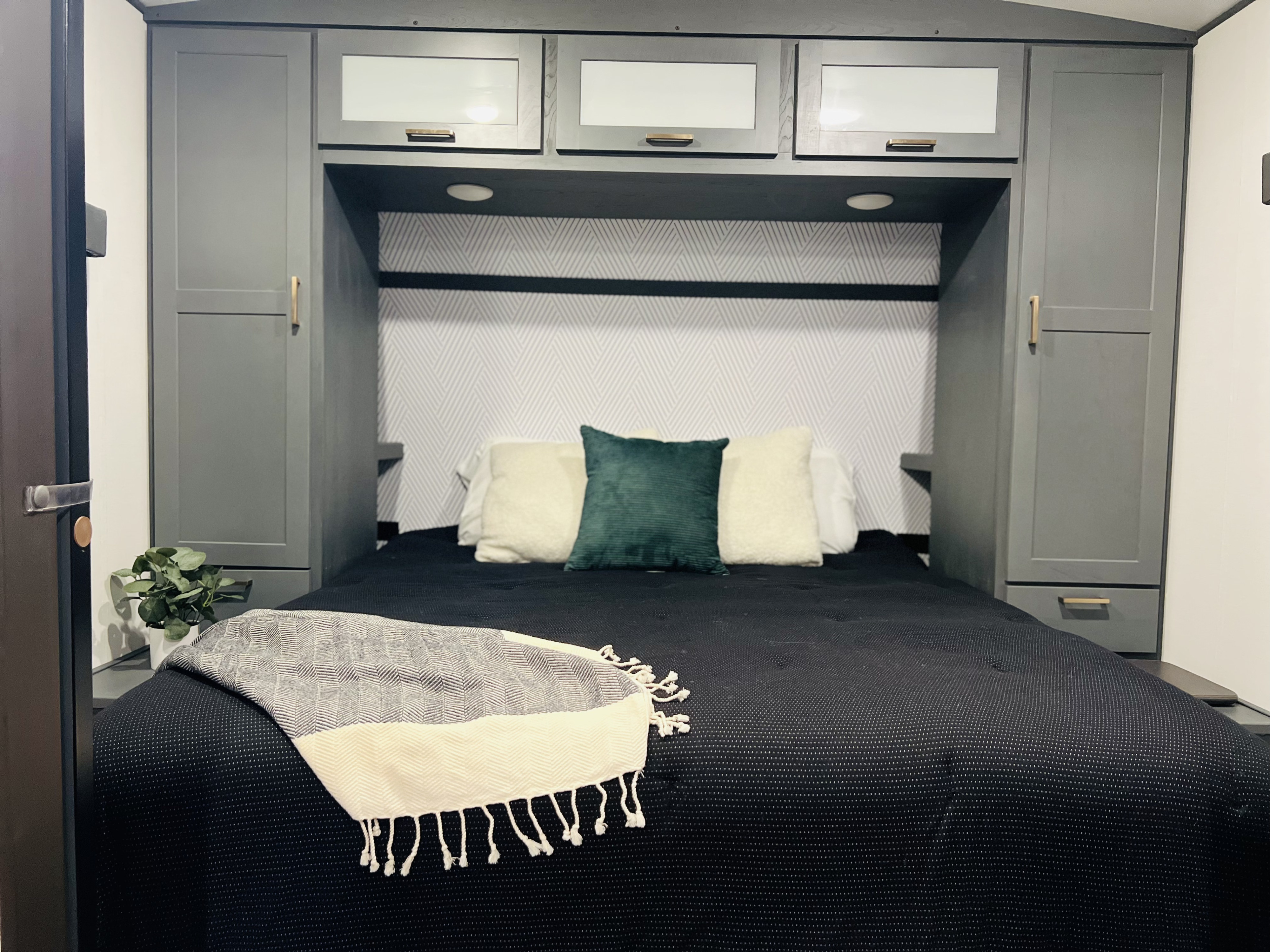 Modern RV rental bedroom featuring sleek gray cabinets, geometric headboard wallpaper, a plush black bed, and cozy throw blanket.. Keystone Bullet 2022