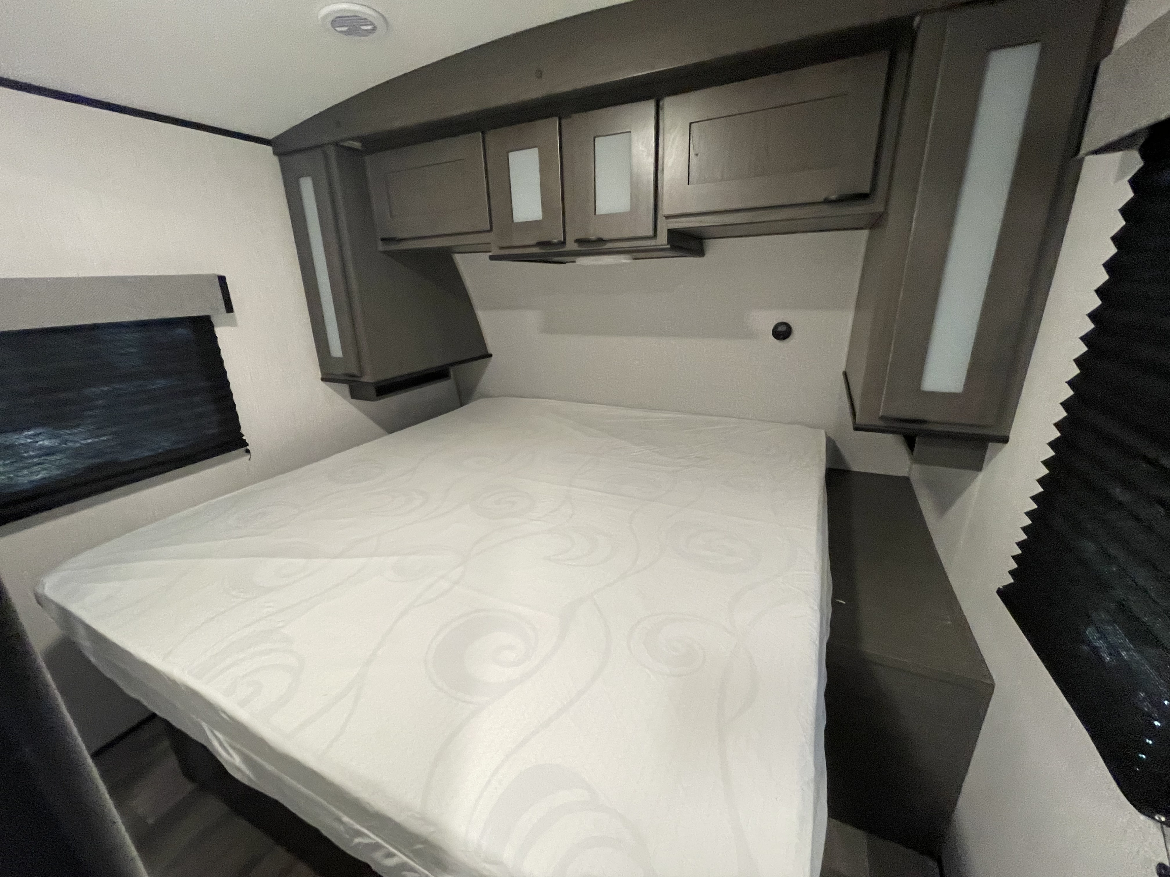 RV rental bedroom: a comfortable white bed, modern overhead cabinets, and a window with shade.. Heartland Mpg 2022