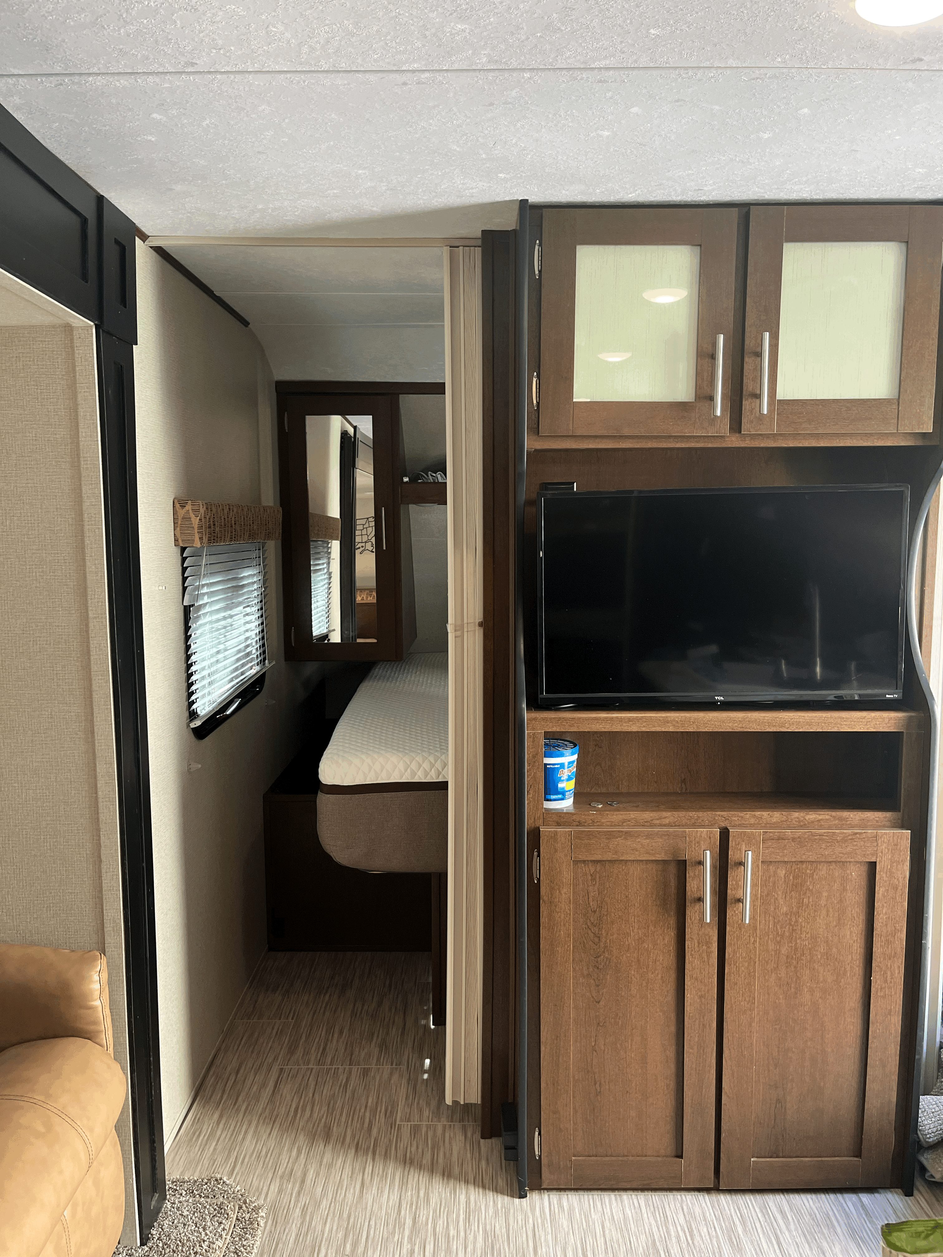 Modern RV rental interior showing a bedroom with a bed & window, plus living area with TV & cabinets.. Forest River Acadia 2018