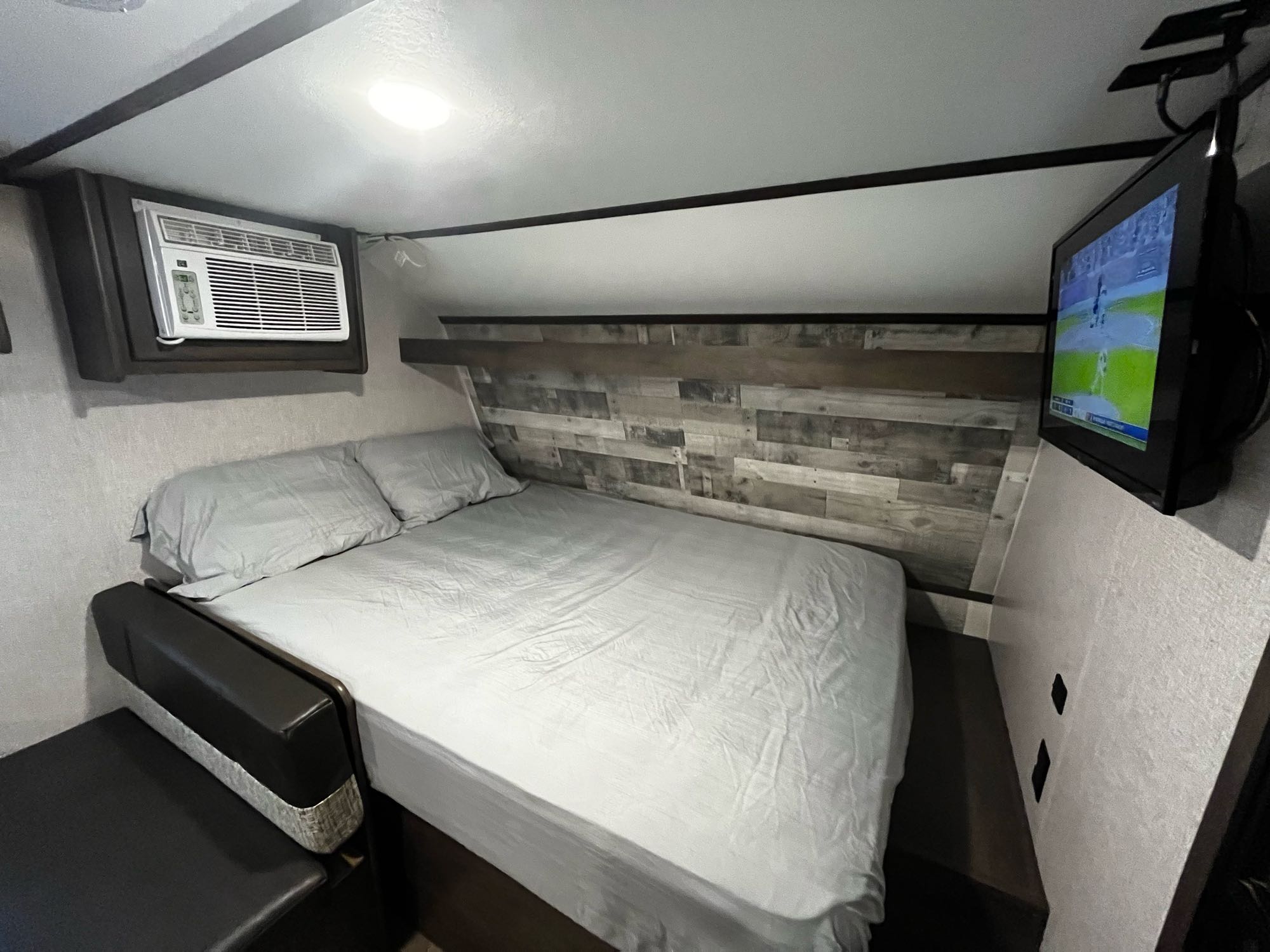 **RV rental**: A compact bedroom featuring a bed with gray linens, wall-mounted AC, and TV for a comfortable stay.. Coleman CM17B21 2021