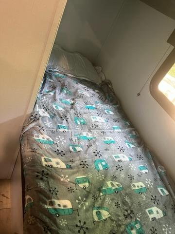 This RV rental's cozy sleeping area features a unique blanket with vintage camper designs.. Forest River 1760bh 2022