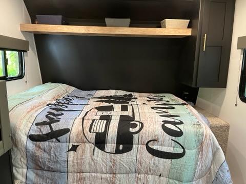 Inside an RV rental: a comfortable bedroom with a camping comforter, dark accent wall, and storage.. Forest River 1760bh 2022