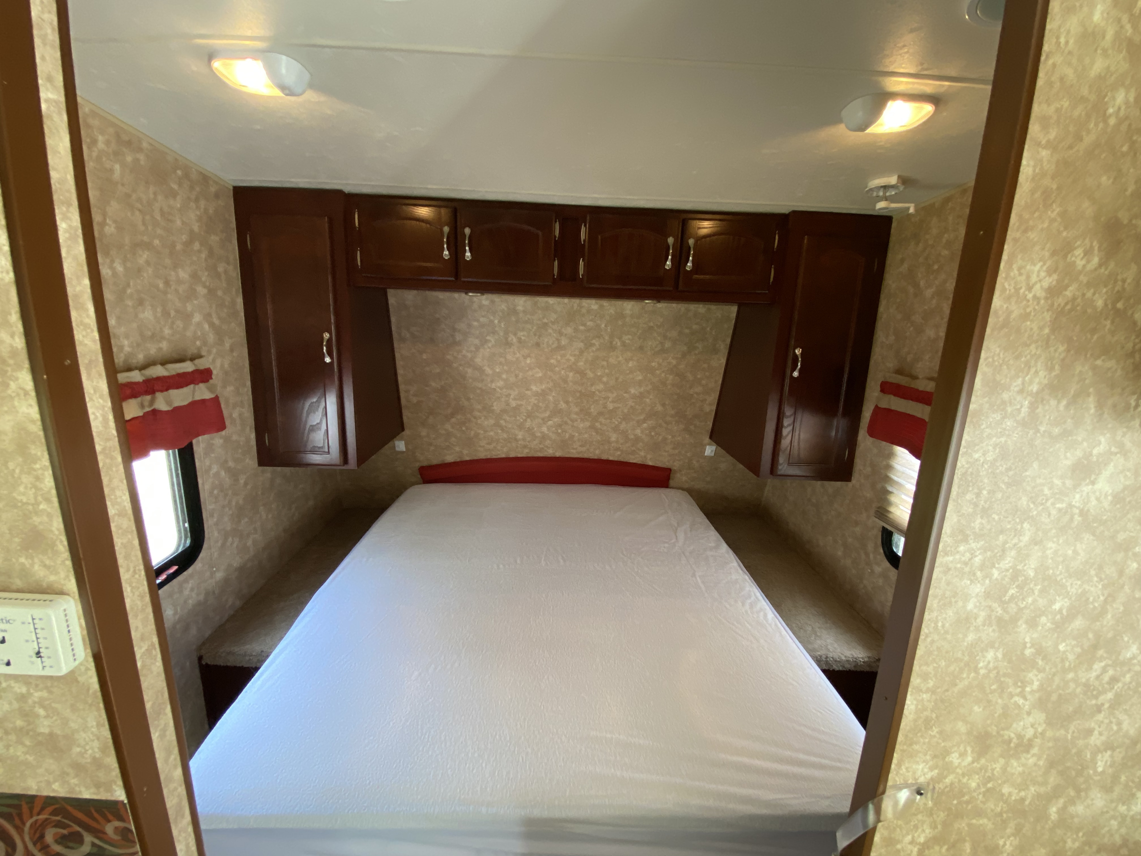 Interior of an rv rental bedroom, featuring a queen bed, dark wood overhead cabinets, and windows.. Other Other 2009