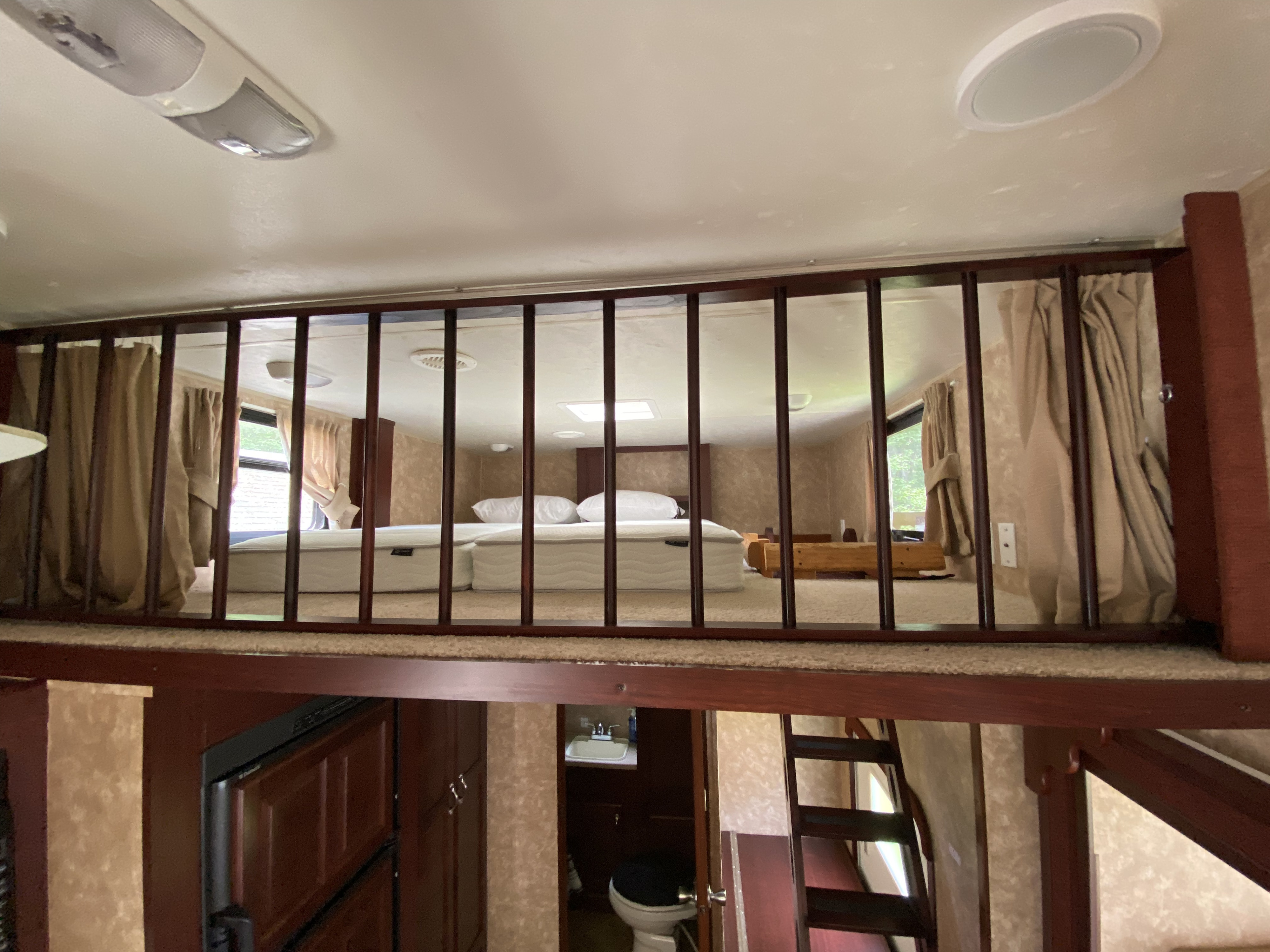 Cozy RV rental loft bedroom with mattress, viewed from below through a wooden railing. Compact bathroom & living space are visible.. Other Other 2009