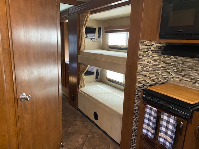 RV rental interior: bunk beds with TVs & windows, alongside a compact kitchen featuring a stove, microwave, and tiled backsplash.. Thor ACE 2015
