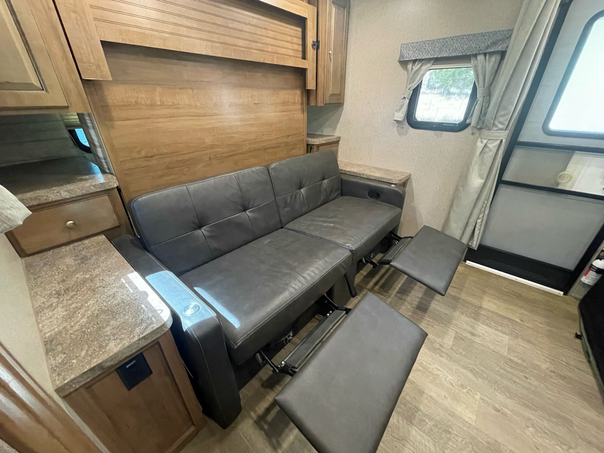 Experience this RV rental's cozy interior, featuring a grey reclining sofa with footrests out, wood-paneled walls, and cabinets.. Forest River Rockwood Mini Lite 2019