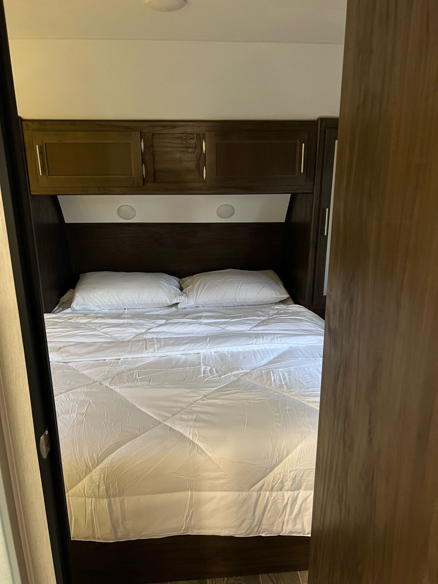 Comfortable RV rental bedroom featuring a bed with white bedding, overhead storage cabinets, and bright interior lighting.. Forest River Cherokee Grey Wolf 2019