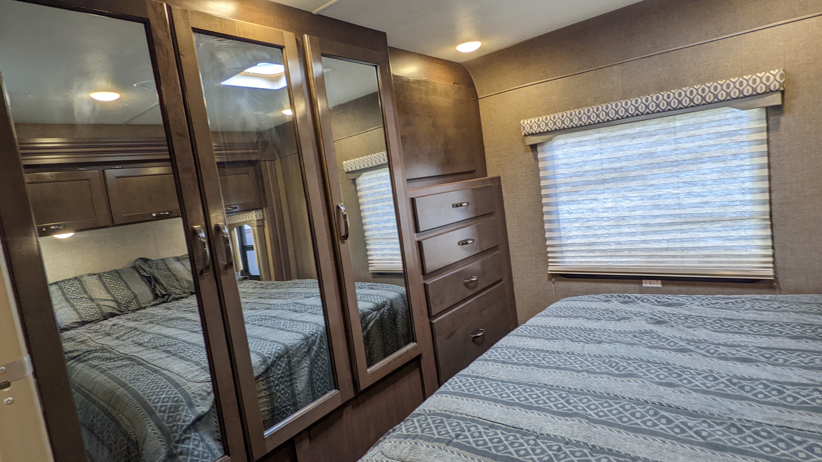 Cozy RV rental bedroom featuring a patterned bedspread, mirrored closet, dresser, and window with blinds.. Thor Freedom Elite 2017