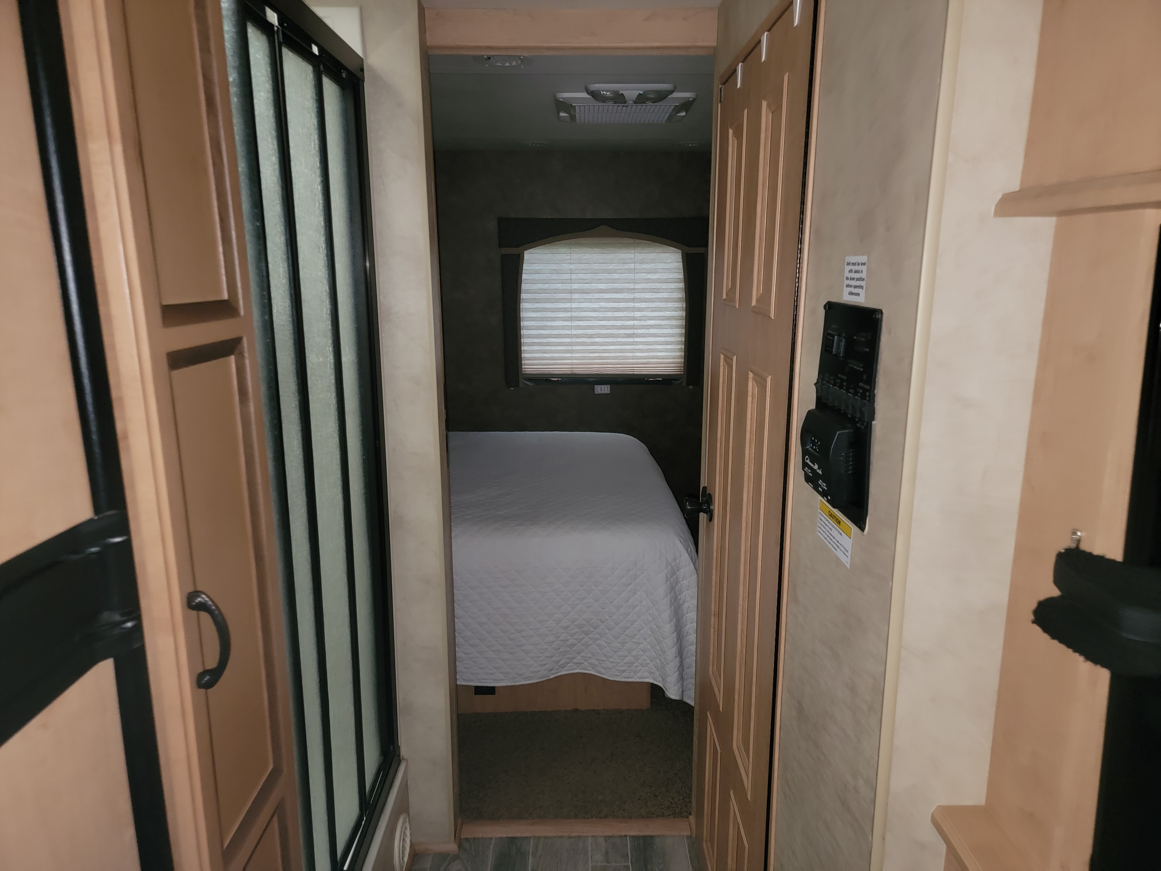 View inside an RV rental: Compact living space with a bright bedroom, shower stall, and system control panel on the wall.. Thor Hurricane 2012