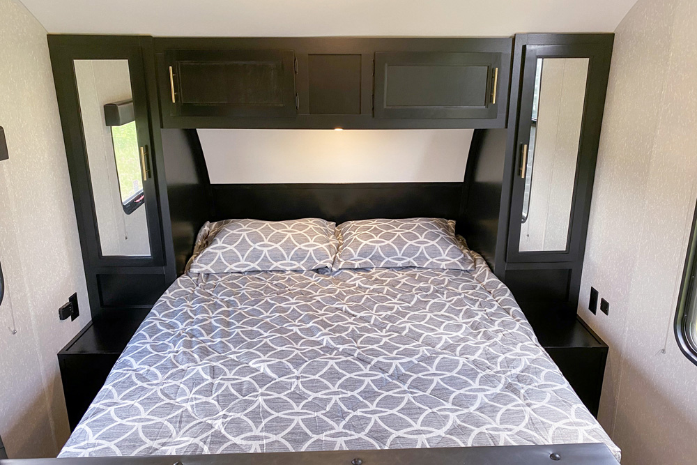 Cozy RV rental bedroom featuring a full-size bed with geometric patterned bedding, black overhead cabinets, and mirrored wardrobes.. Forest River Cherokee Greywolf 2022