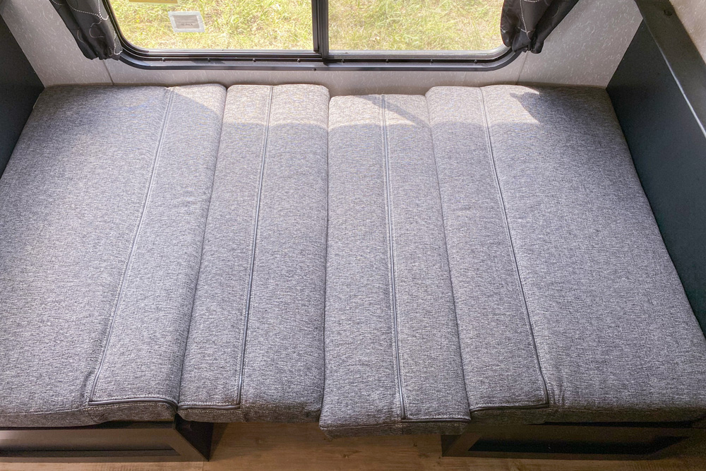 Comfortable grey cushion bed/dinette setup inside an RV rental, perfect for sleeping or lounging on your trip.. Forest River Cherokee Greywolf 2022