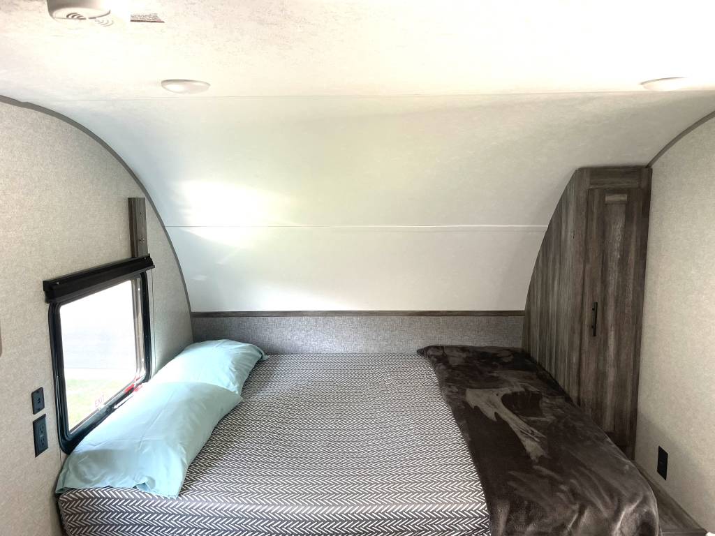 Step inside this RV rental bedroom featuring a full bed, window, and built-in storage. Ideal for road trips.. Forest River Wildwood FSX 2020