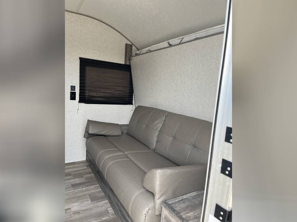RV rental interior: Grey sofa, window with dark blind. A light panel above hints at a fold-down bed for flexible sleeping.. Forest River Wildwood FSX 2020