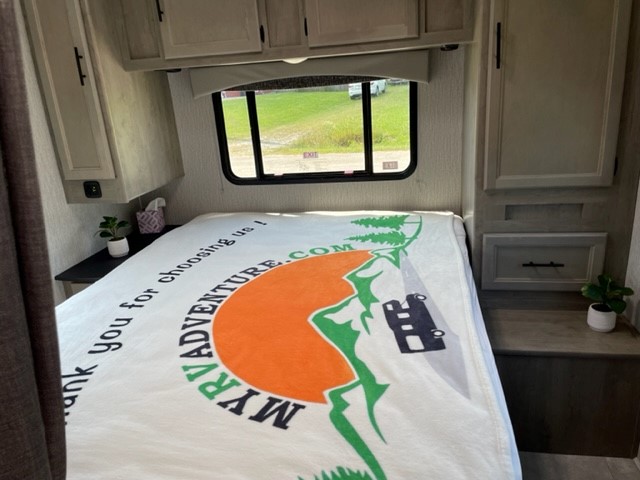Experience comfort in this RV rental bedroom, complete with a cozy bed and "MYRVADVENTURE.COM" blanket.. Coachmen Freelander 2022