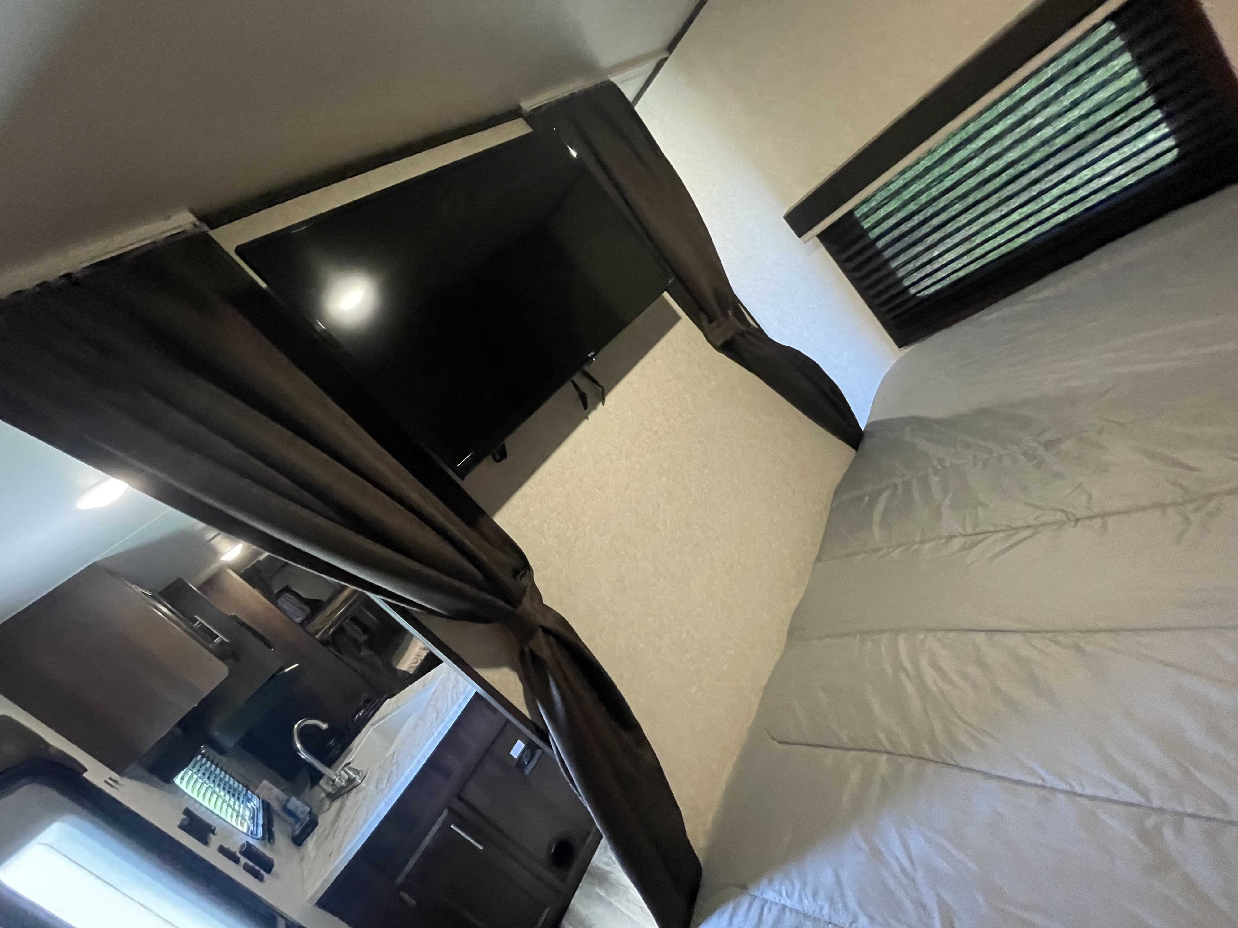 Inside an RV rental: a compact living space featuring a bed, window, mounted TV, and a small kitchen with a sink.. Jayco Jay Flight SLX 2019