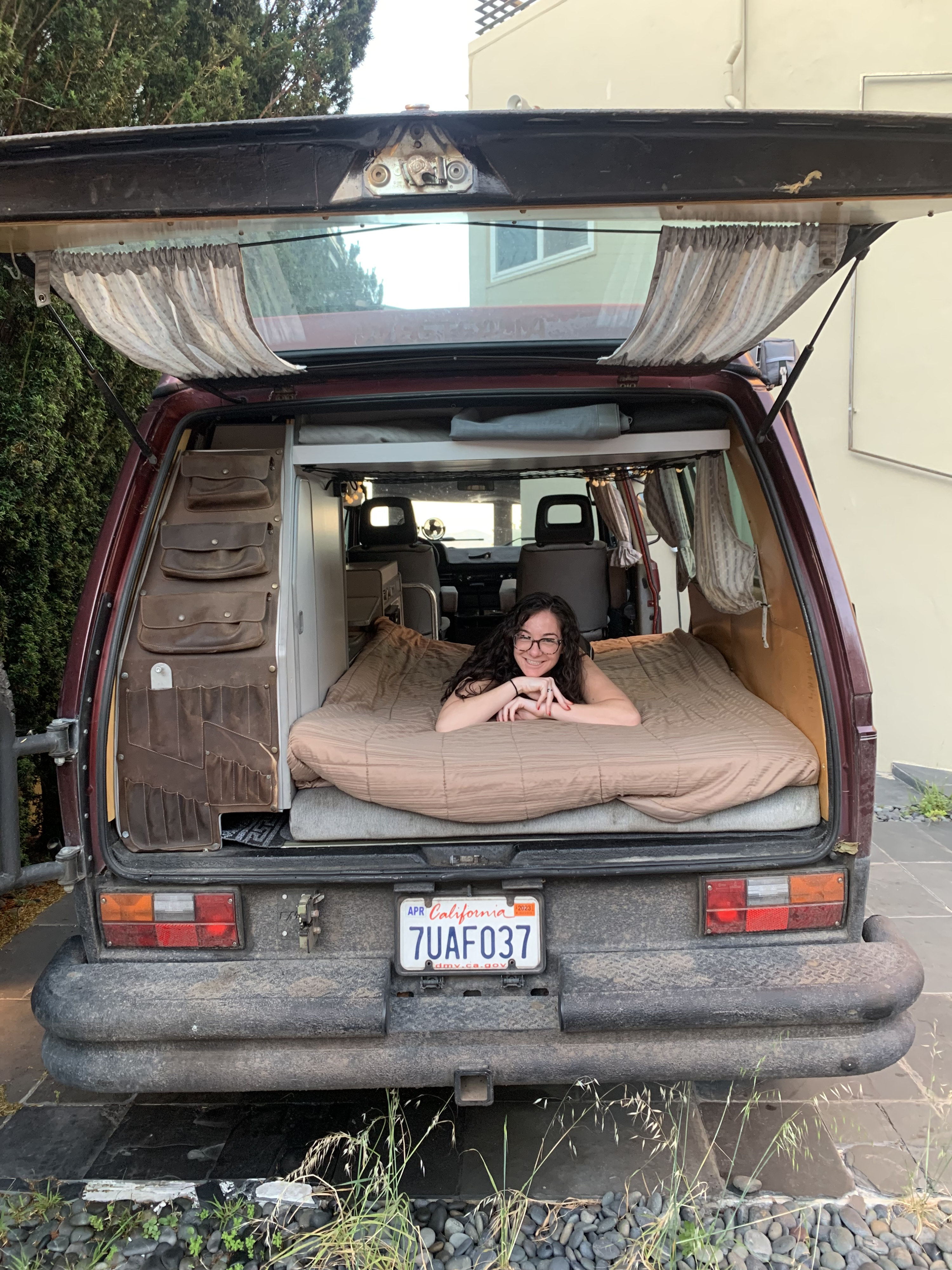 Classic camper van rear view, featuring a smiling woman relaxing on a bed. Great for your next RV rental road trip!. Volkswagen Westfalia 1987