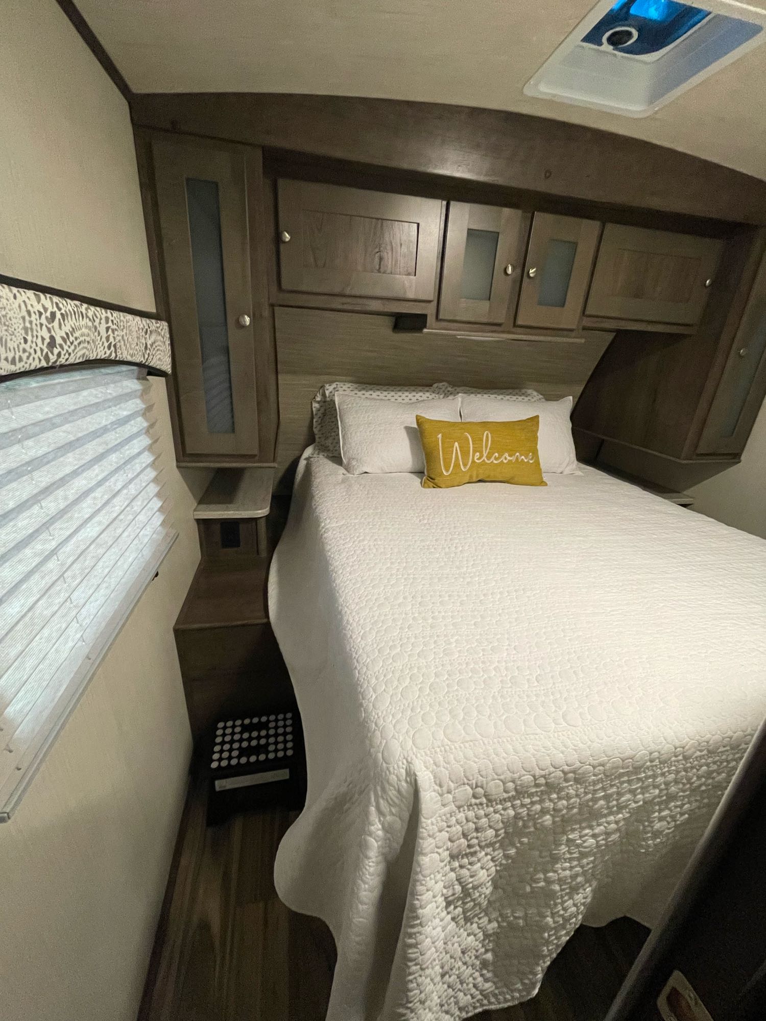 Cozy RV rental bedroom featuring a comfortable bed with a "Welcome" pillow, overhead storage, and window blinds.. Cruiser RV MPG Ultra Lite 2019