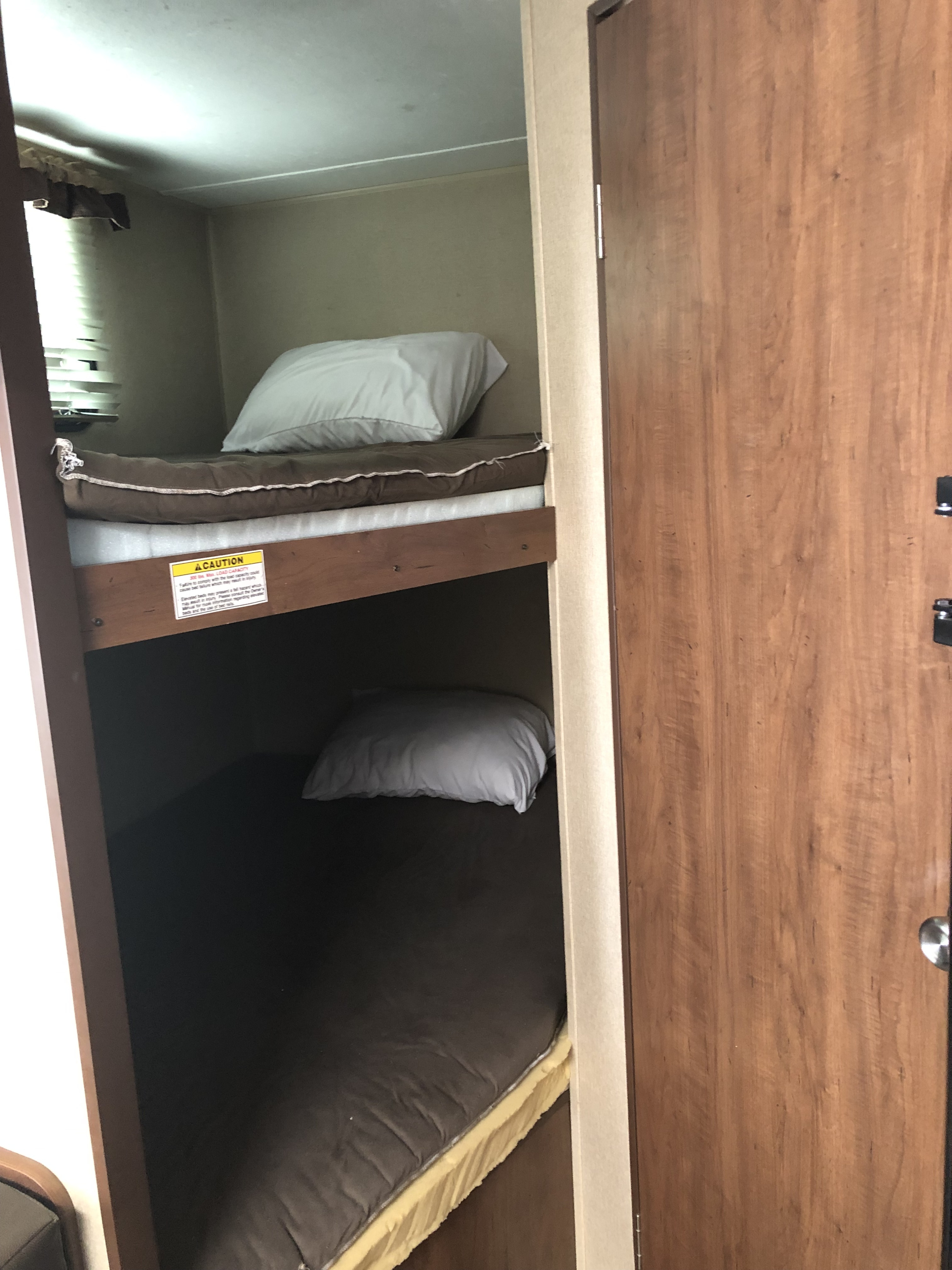 Compact bunk beds within an RV rental, featuring a visible caution sign on the upper bunk for safety.. Dutchmen Dutchmen Trailer 2014