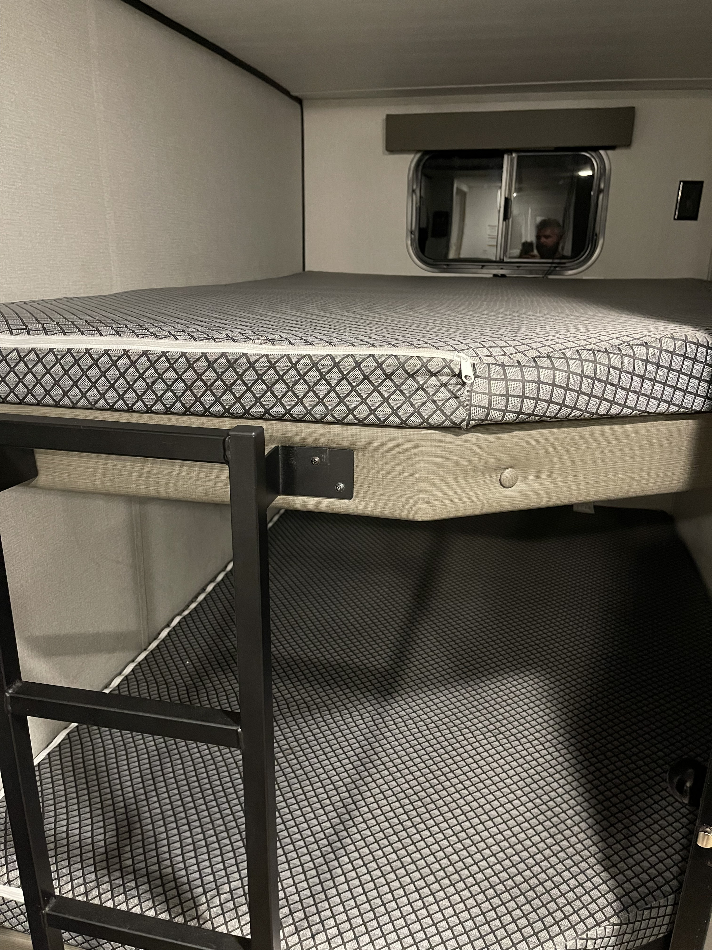 Clean RV rental interior showing bunk beds. The upper bunk has a patterned mattress, accessed by a ladder. A window is above.. Keystone Hideout 250BH 2022