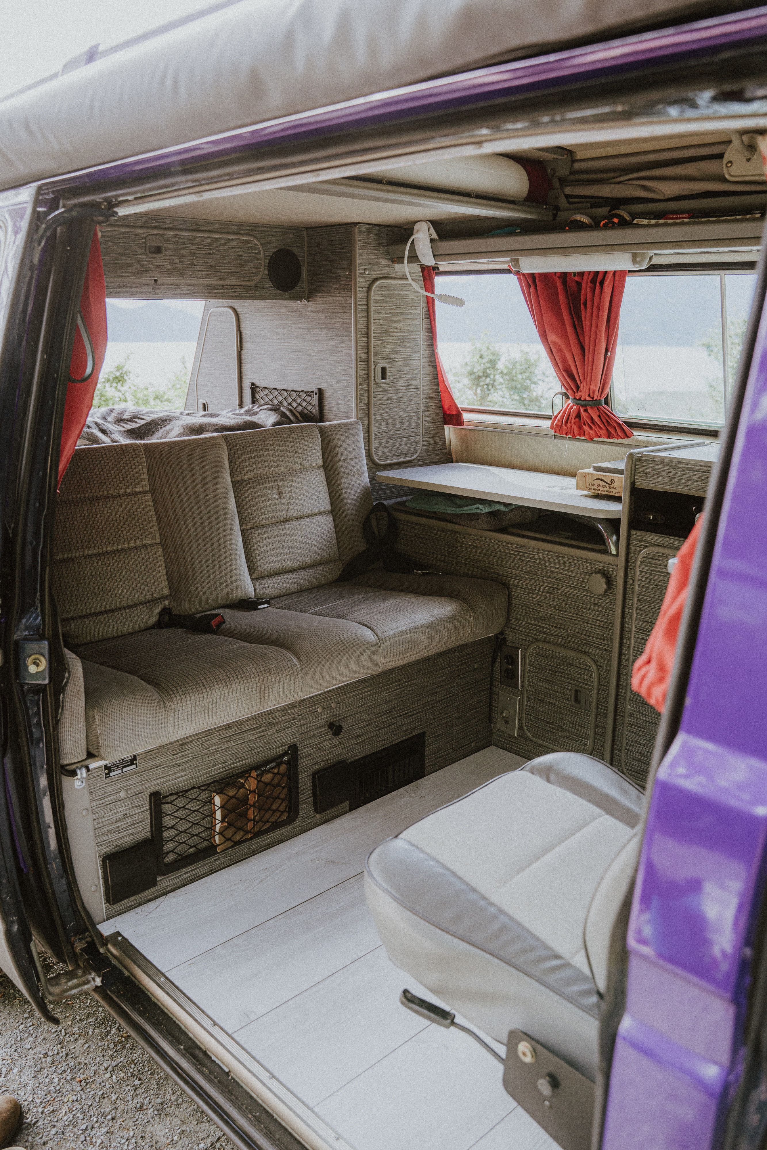 Inside a vibrant purple camper van, an RV rental with comfortable rear seating, a cozy bed, and a compact kitchen setup.. Volkswagen Vanagon 1991