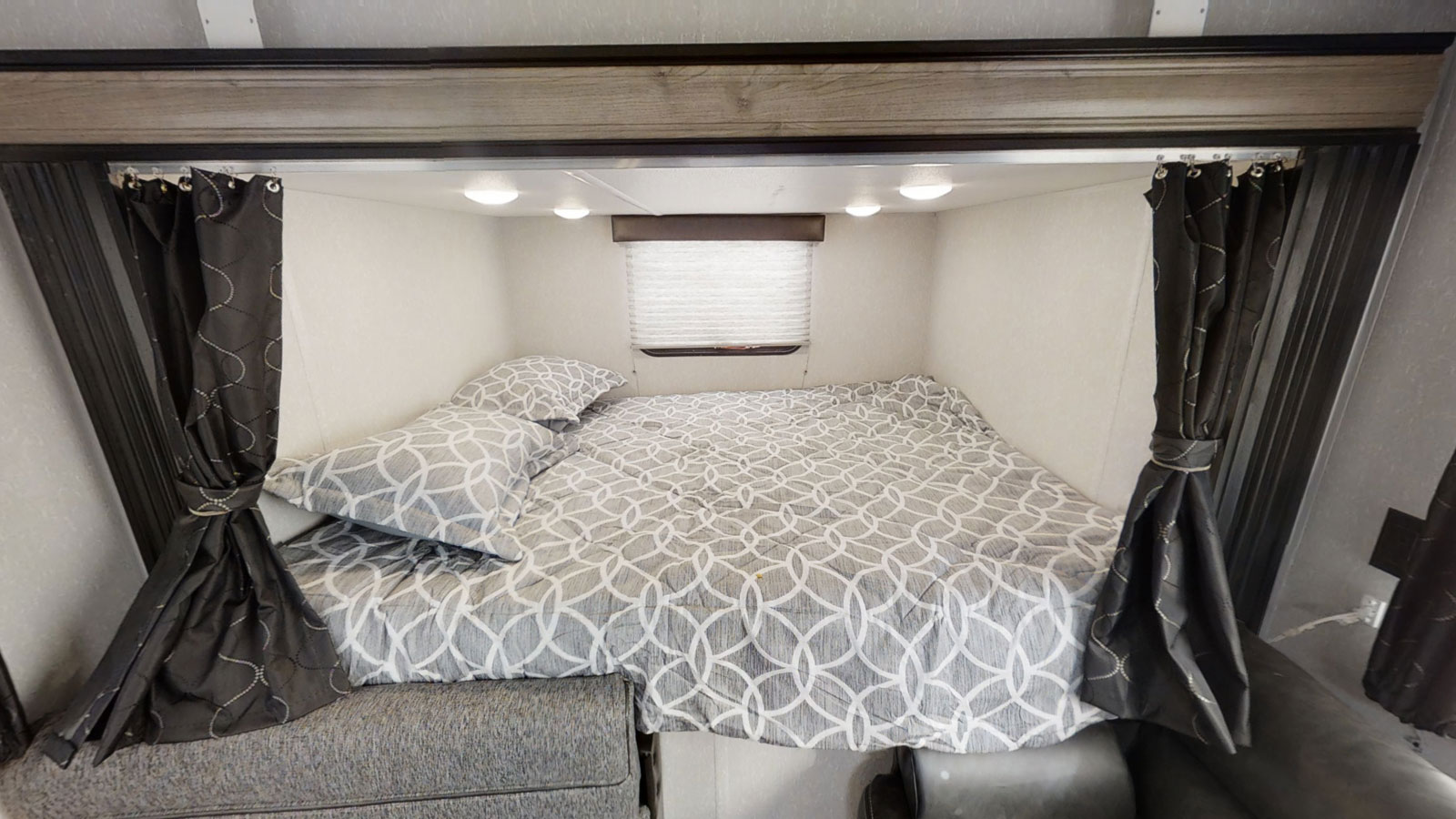 Cozy RV rental bedroom featuring a patterned bed, overhead lighting, and tied-back privacy curtains.. Forest River Cherokee Grey Wolf Special Edition 2020