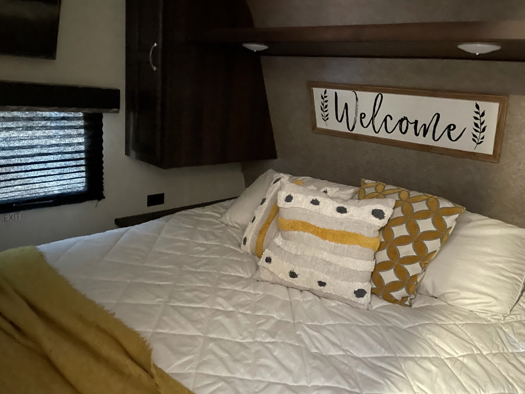 Step inside this inviting RV rental bedroom with a comfy bed, white and yellow accents, a 'Welcome' sign, and overhead storage.. Jayco Jay Flight 2018