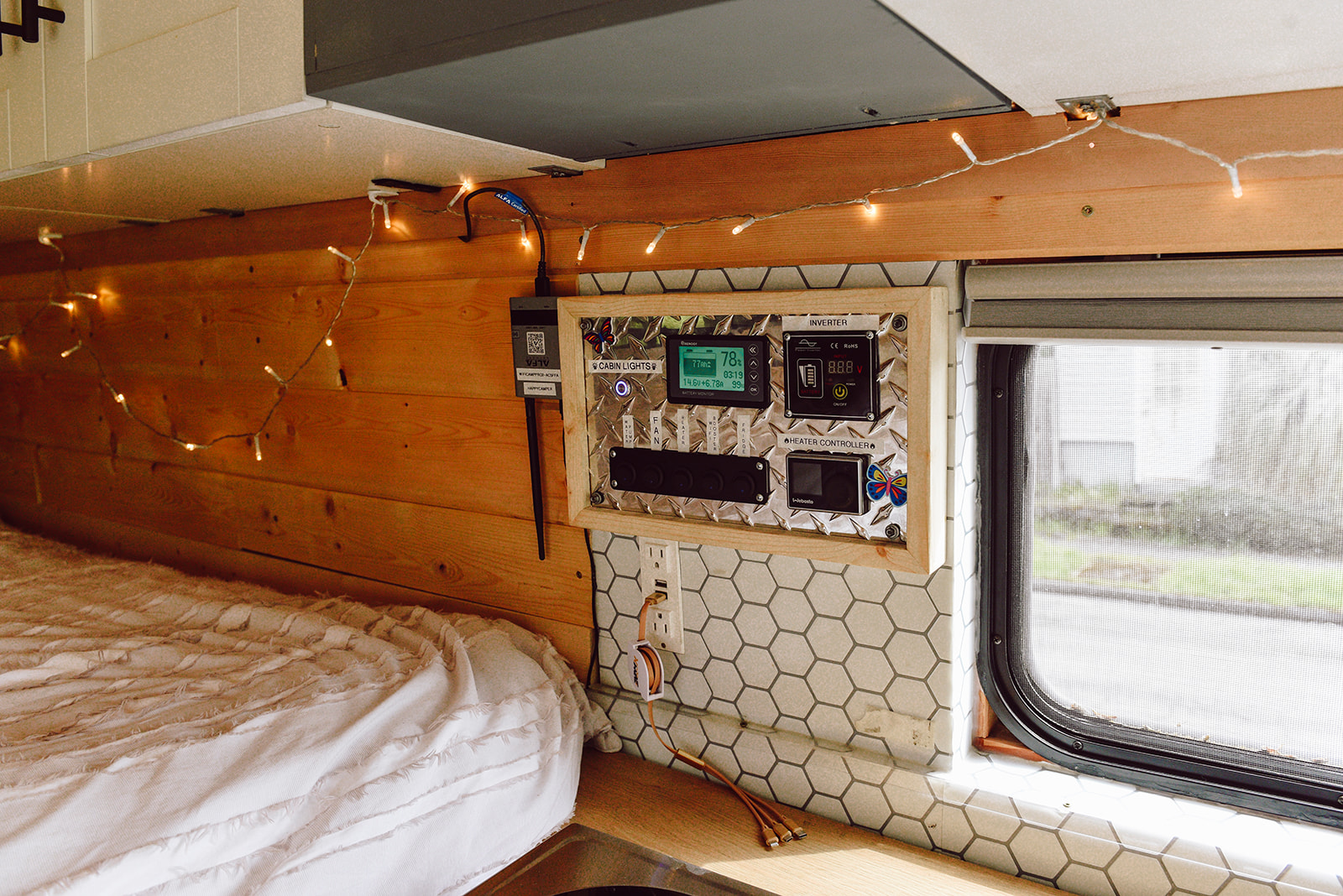 Inside an RV rental: custom campervan control panel for power/heating, cozy string lights, bed, and window view.. Other Other 2016