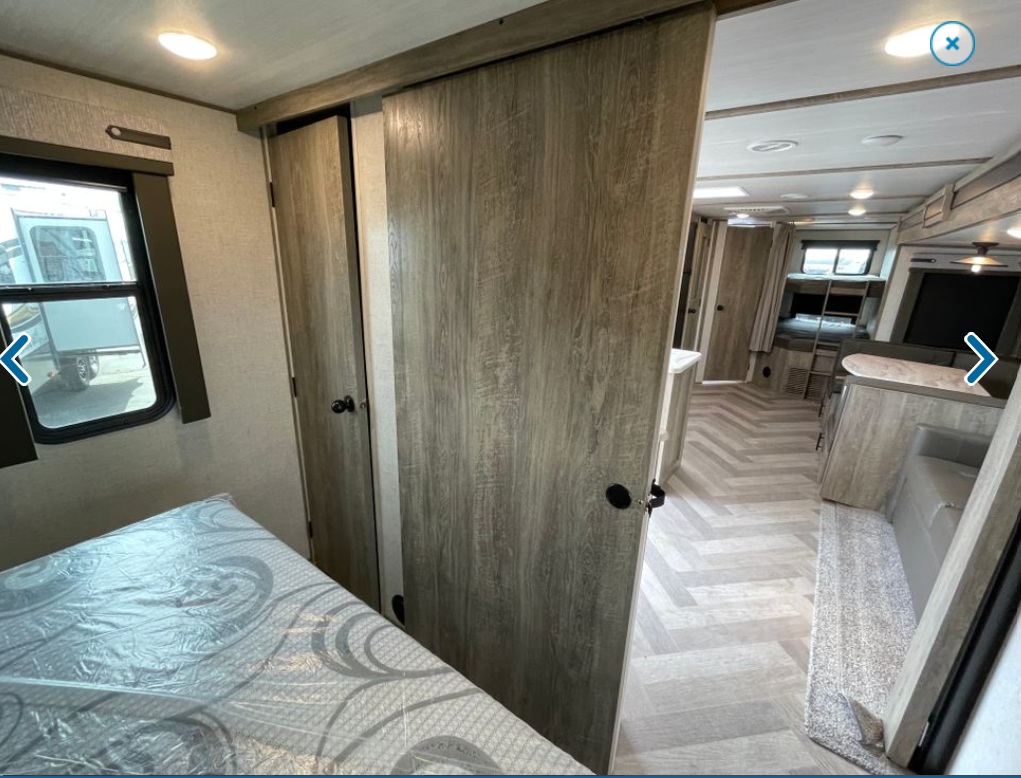 Interior view of a modern RV rental, showing a bedroom with a bed & sliding doors, opening to a living area with bunk beds.. Forest River Wildwood Heritage Glen 2022