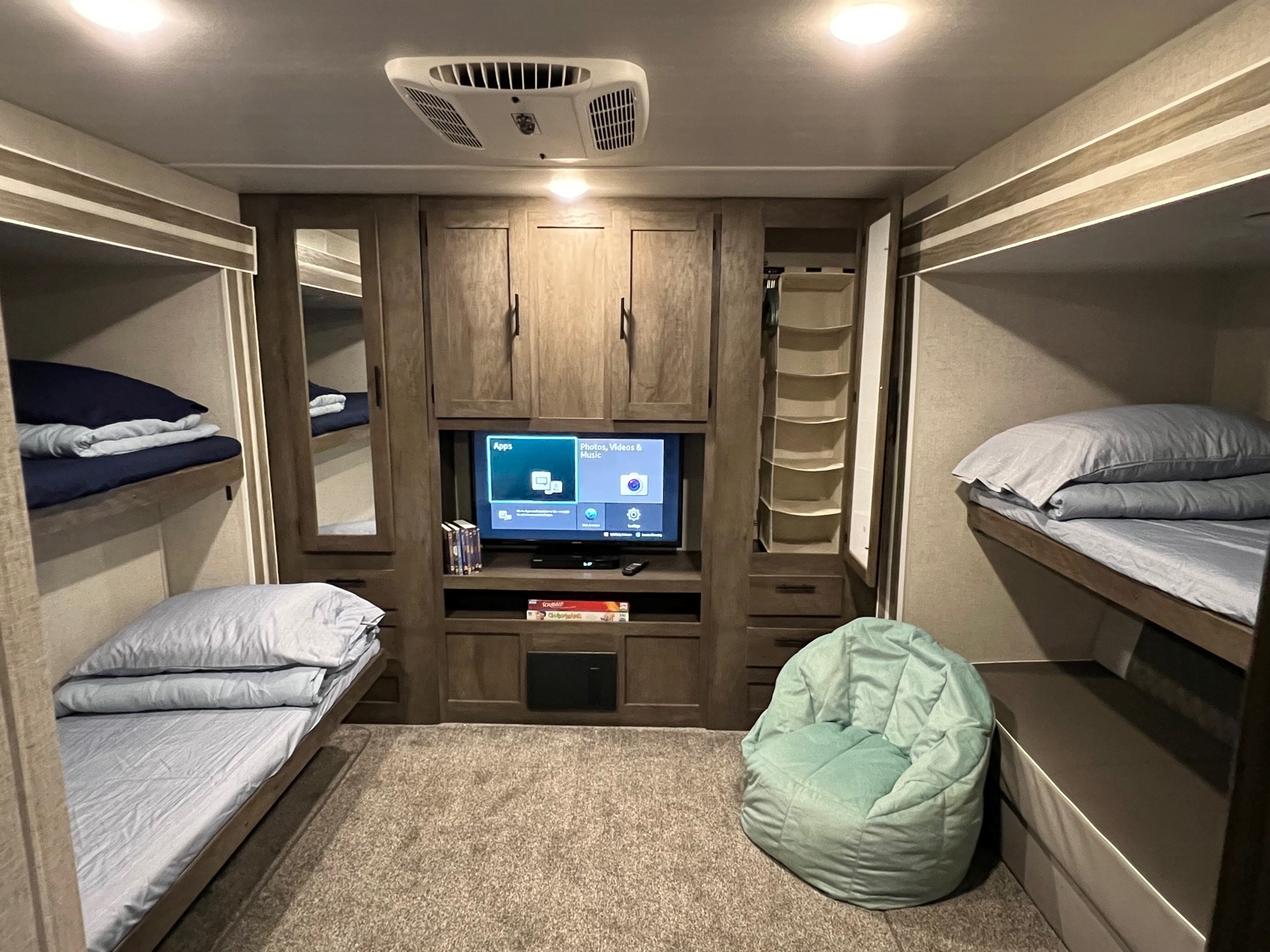 Spacious RV rental bunkhouse with light wood cabinetry, dual bunk beds, central TV, & cozy beanbag chair.. Forest River Wildwood 2021