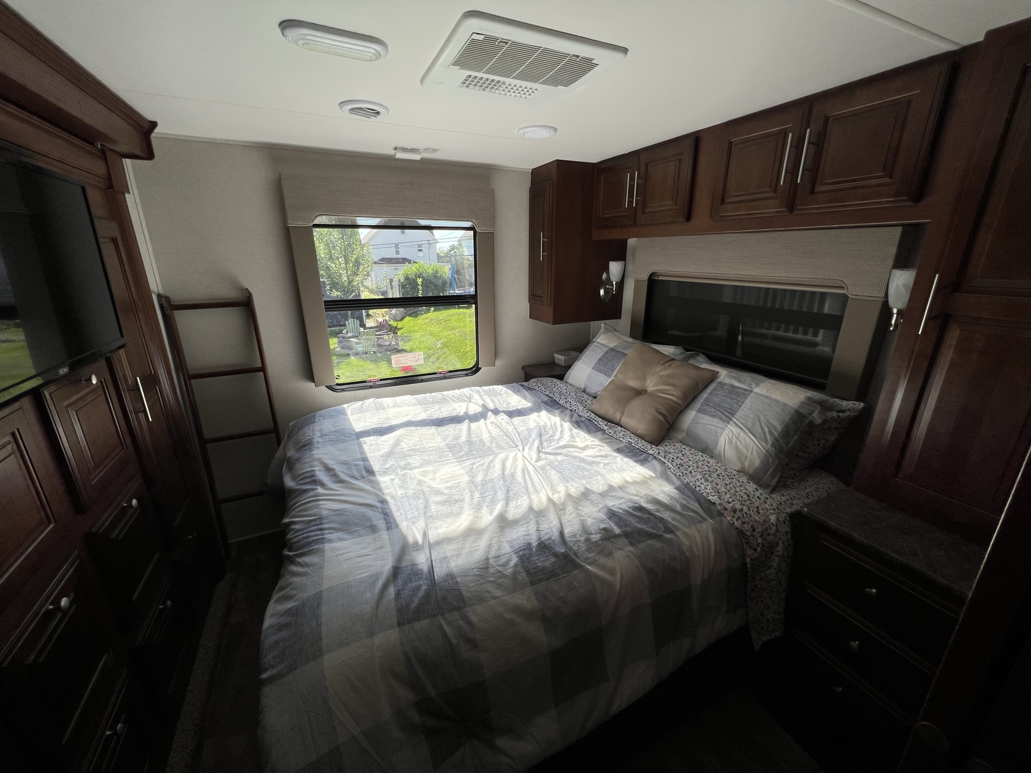 Cozy RV rental bedroom featuring a plaid bed, dark wood storage, TV, and sunlit window with a view outside.. Georgetown 351 DS Bunkhouse 2017