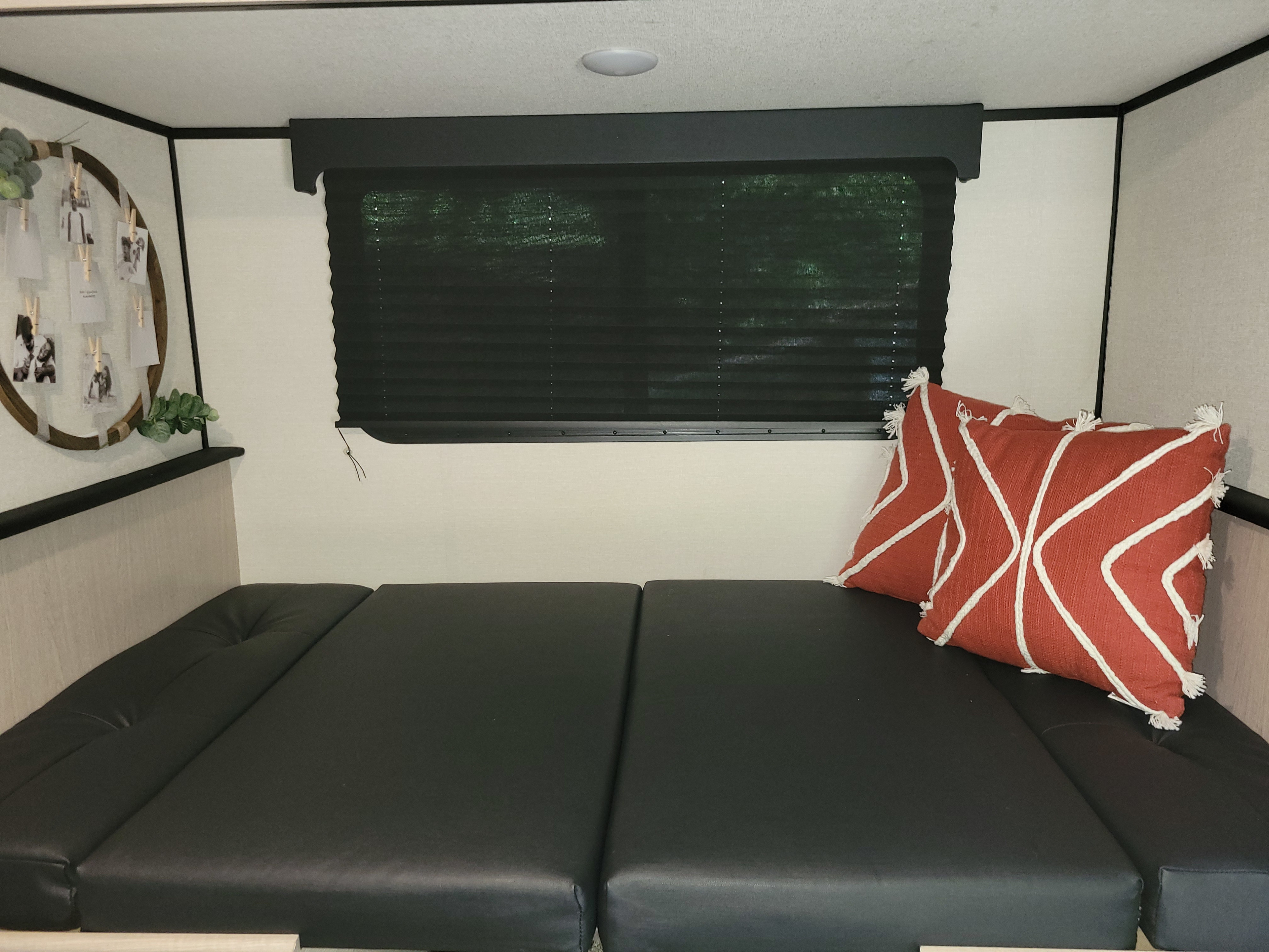 Cozy RV rental sleeping area with dark cushions, red accent pillows, a window blind, and personal decor.. Other Other 2022