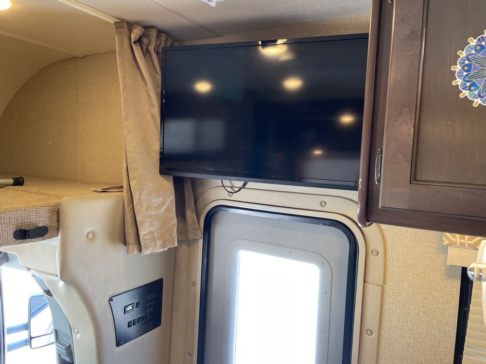 Cozy RV rental interior showing a mounted TV, bunk over cab, and control panel near the main entry door.. Thor Freedom Elite 2018