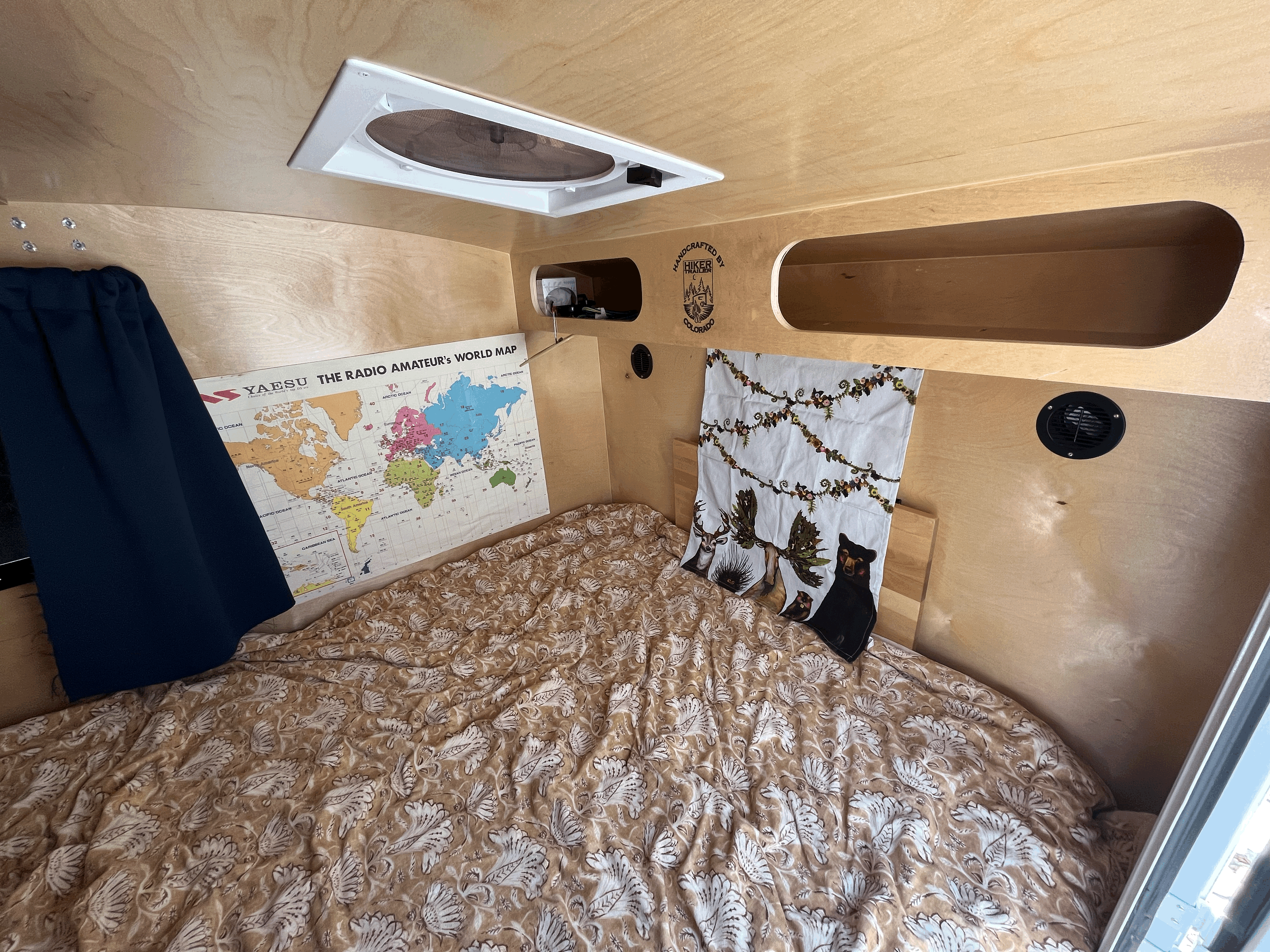 Compact Hiker Trailer RV rental cabin: bed with patterned comforter, amateur radio map, and ceiling fan.. Hiker Trailer Highway Deluxe 2022