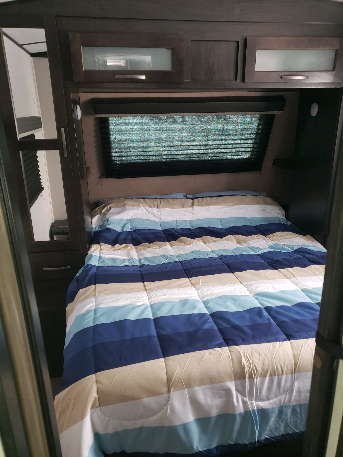 Cozy RV rental bedroom featuring a striped comforter, window with blinds, and overhead storage, ideal for your next adventure.. FOREST RIVER 287BHSS 2020