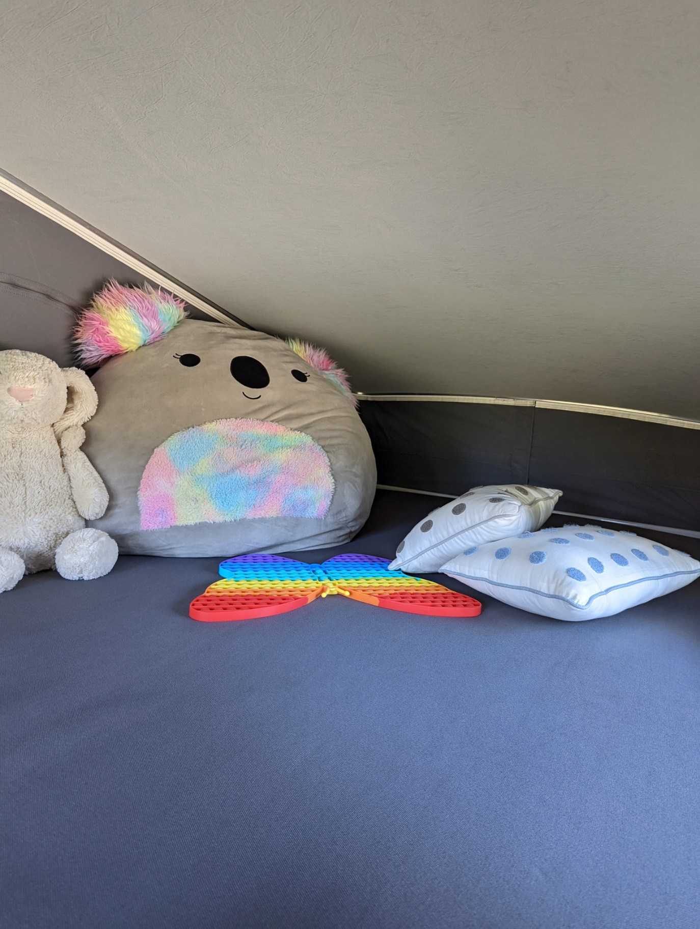 Cozy RV rental bed with a large koala plush, white toy, rainbow pop-it, and two white pillows for comfort.. Winnebago Solis 59P 2023