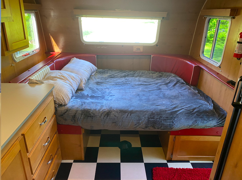 Cozy RV rental interior featuring a spacious bed with red cushions, wood paneling, checkered floor, and bright windows.. Riverside RV Retro 2017