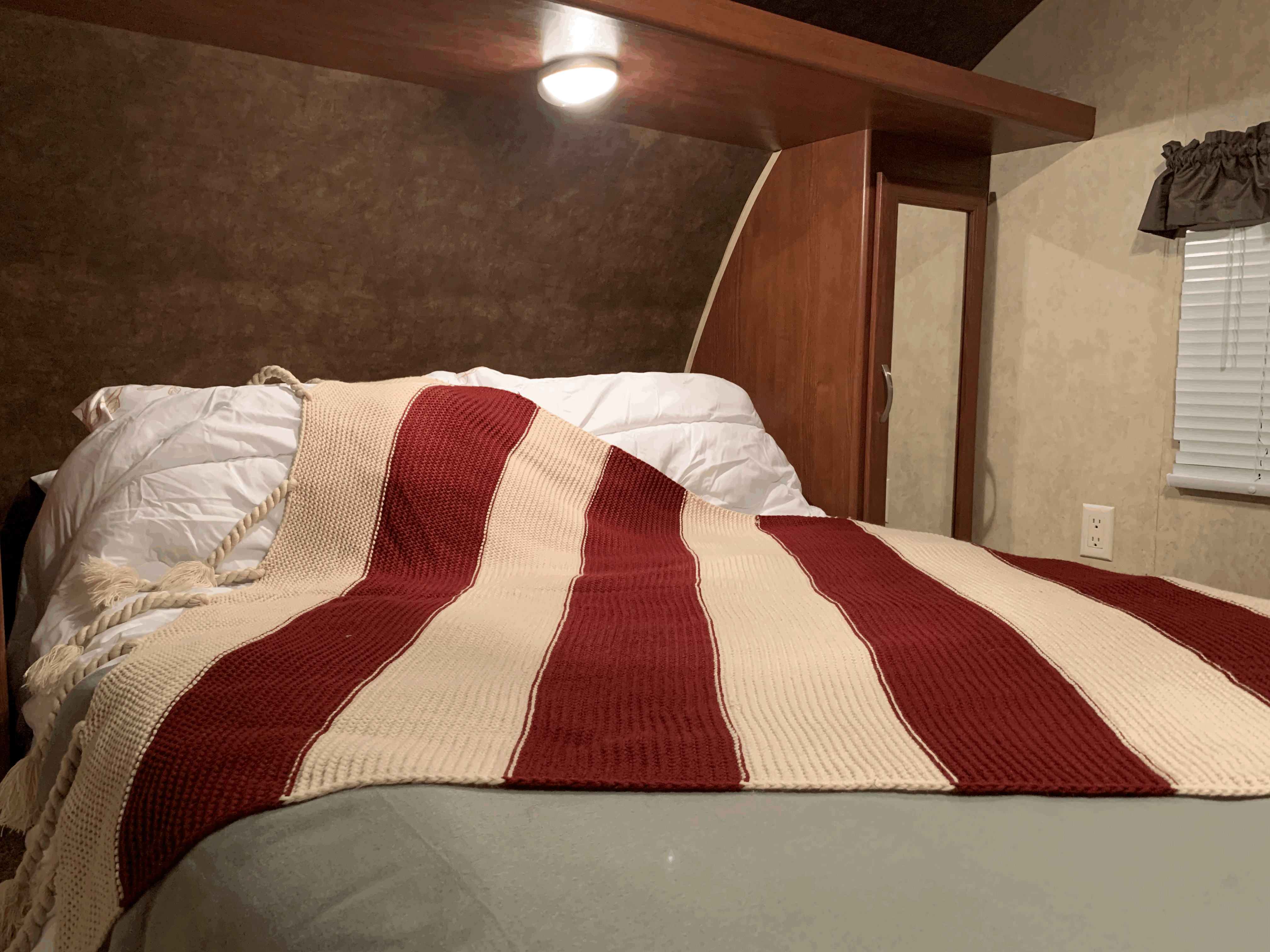 Inside an RV rental: a comfortable bed with white pillows and a bold red and cream striped blanket.. Forest River Wildwood X-Lite 2014
