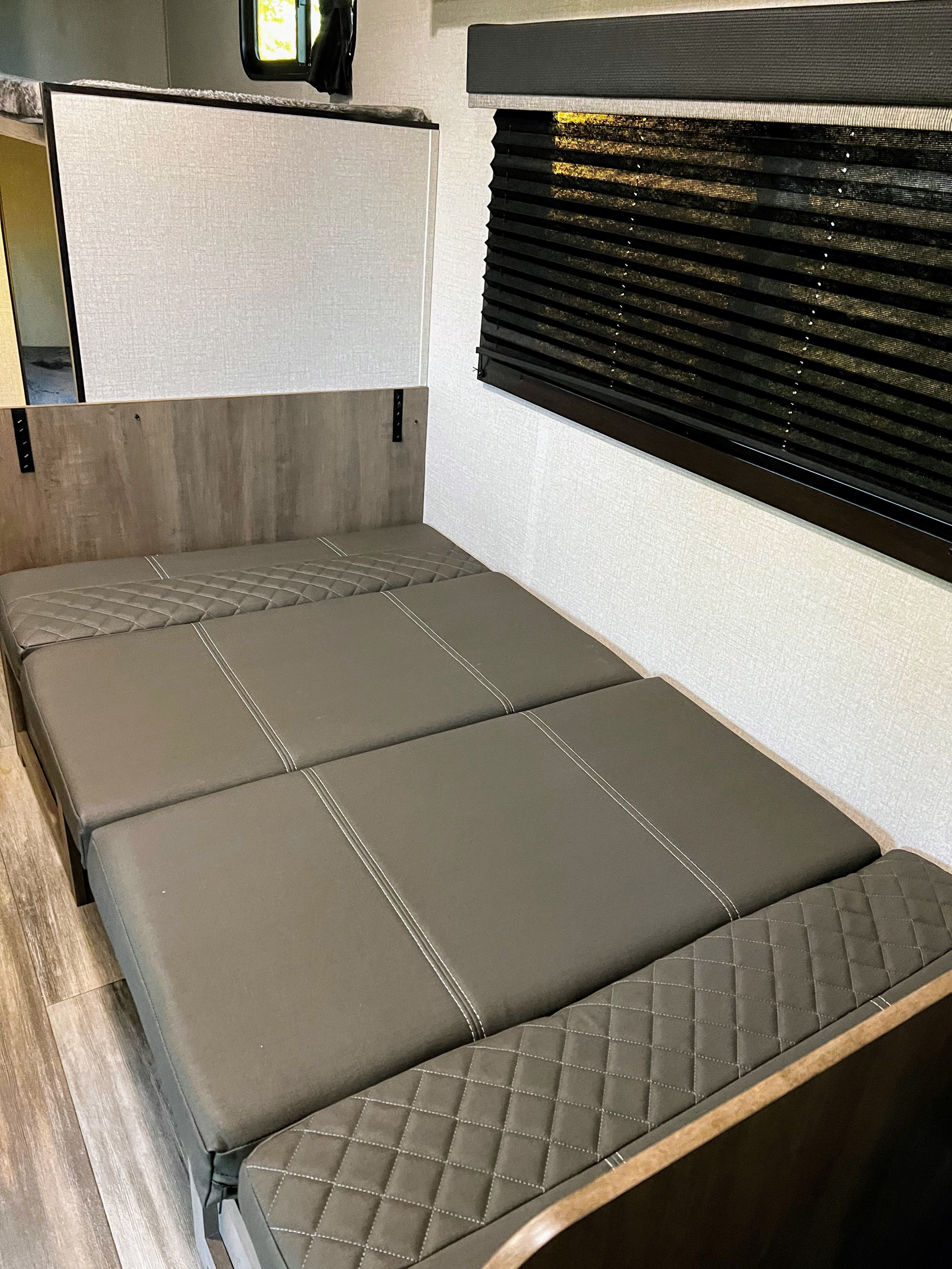 Modern rv rental interior showing a comfortable, convertible gray sofa bed with quilted sections, textured walls, and blinds.. Open Range Open Range 2022