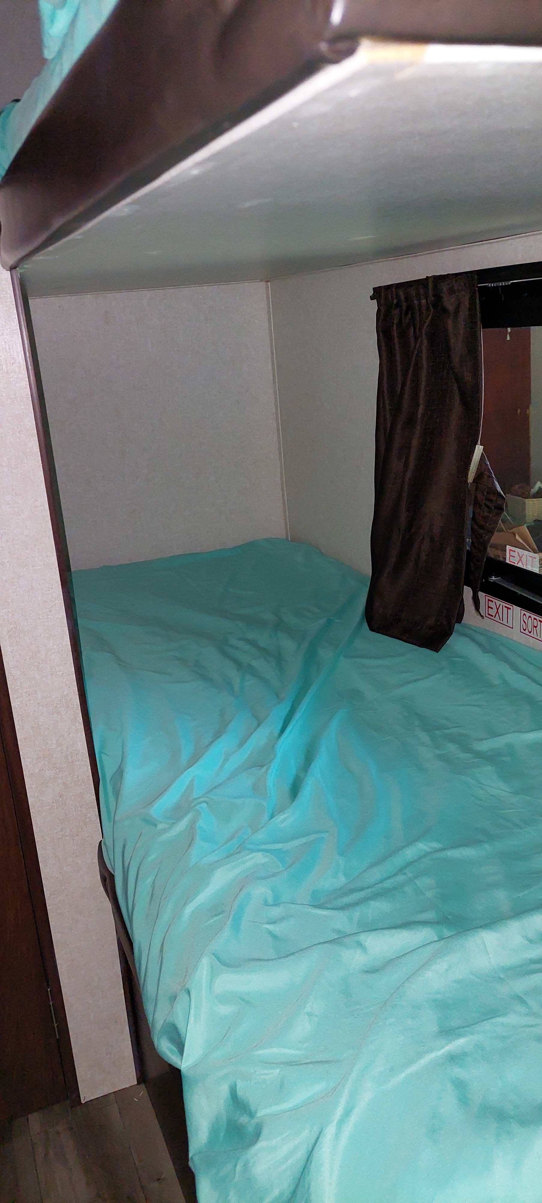 Inside an RV rental: a cozy bunk bed with turquoise bedding, dark privacy curtain, and visible exit signs.. Jayco Jay Flight SLX Baja Edition 2019