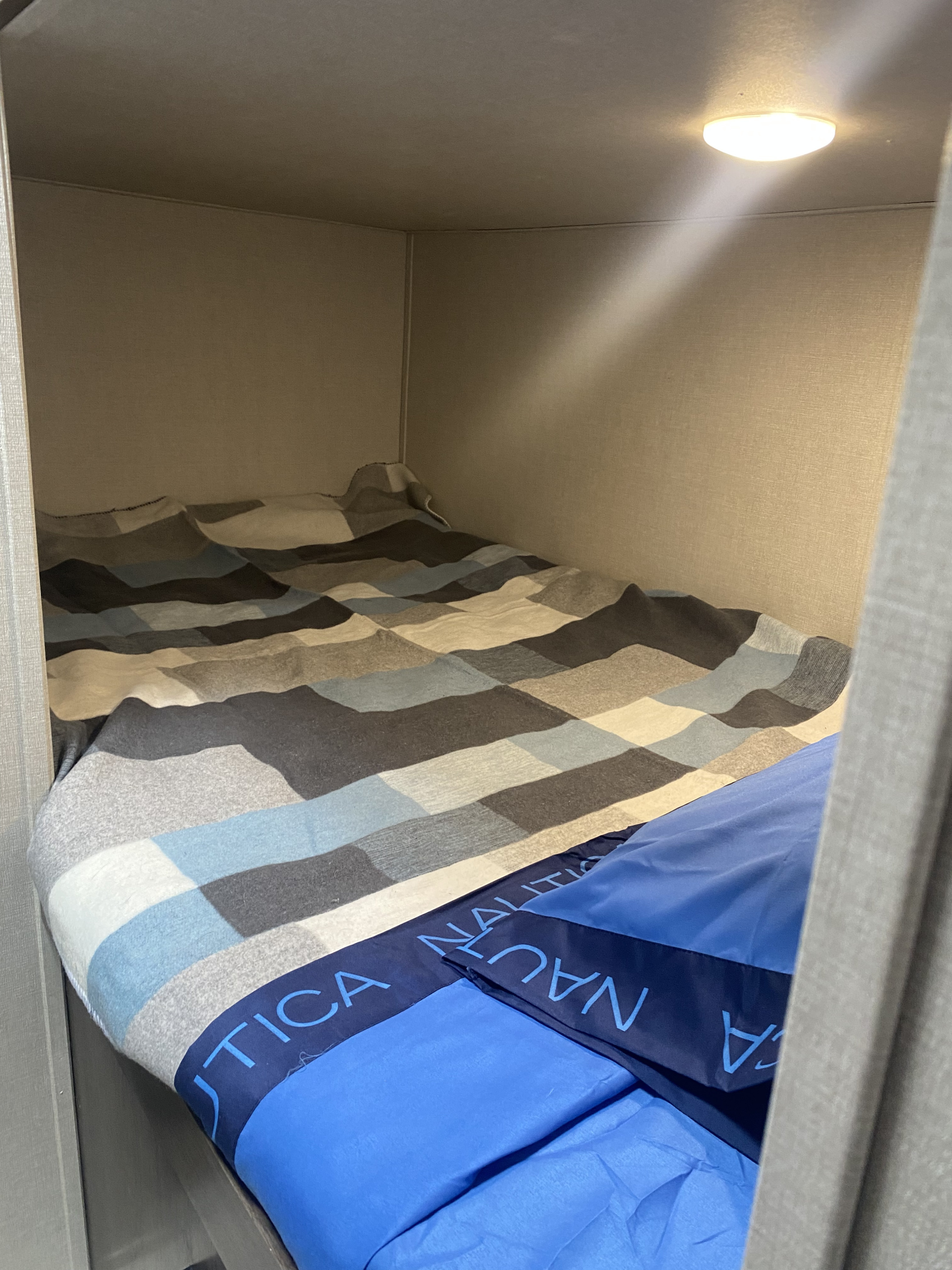 Cozy RV rental bunk bed featuring a blue and gray patterned quilt and a blue Nautica pillow, lit by a ceiling light.. Prime Time Avenger 2021