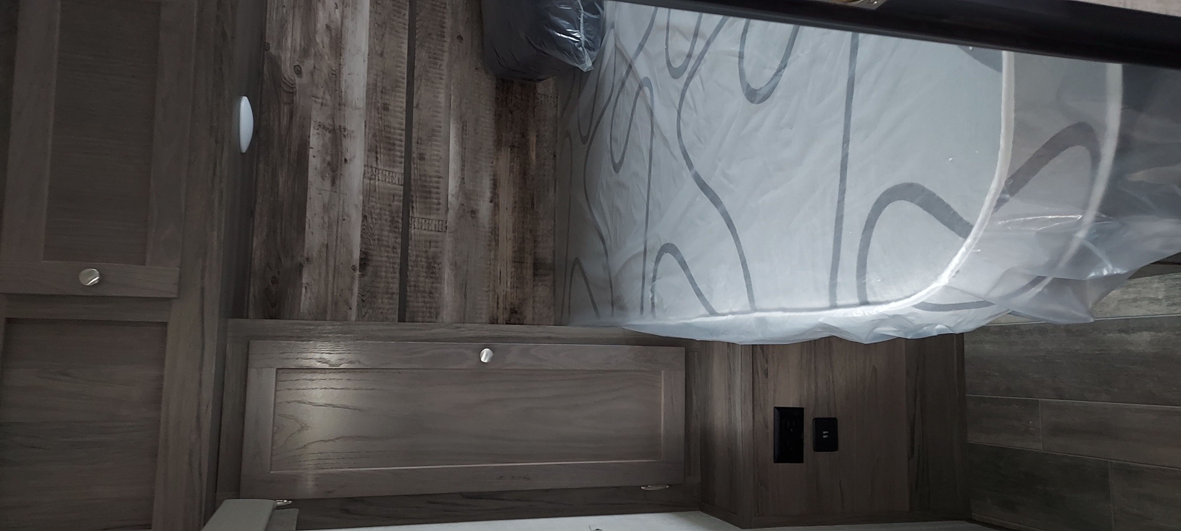 Inside an RV rental: a modern bedroom featuring a bed with a protective plastic cover, wood-paneled walls, and sleek storage cabinets.. Gulfstream Streamlite 28BBS 2022