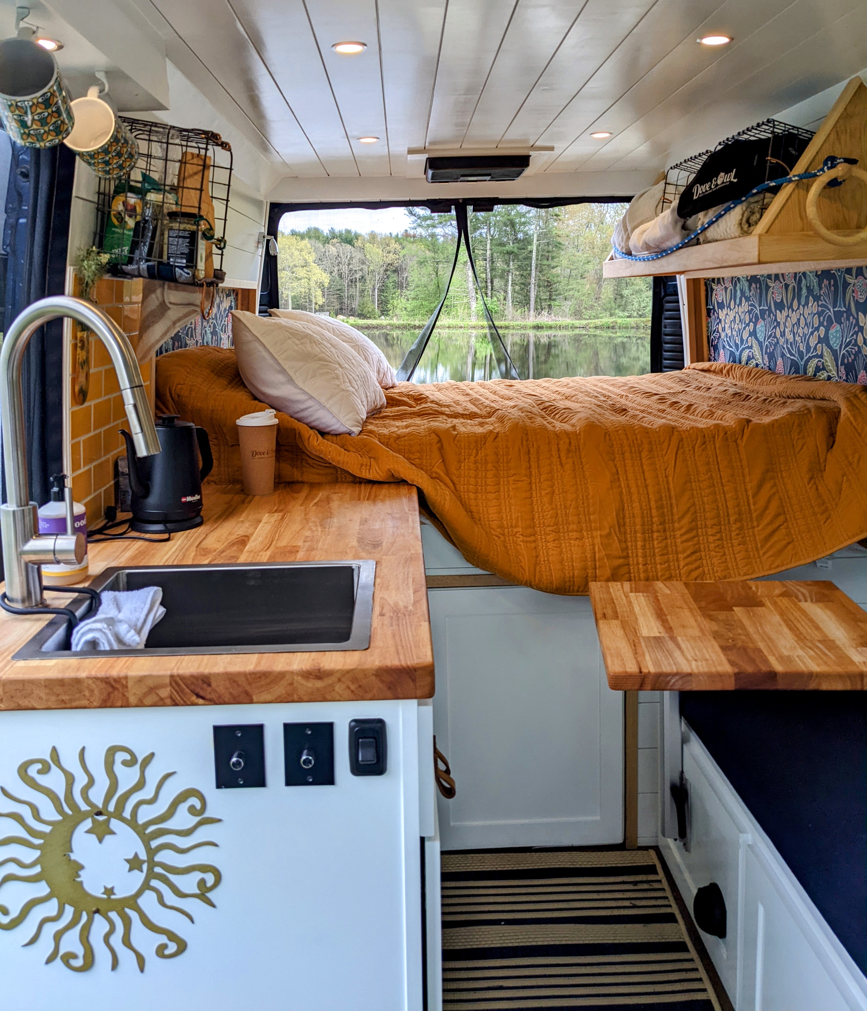 Cozy RV rental interior with bed, kitchen, and scenic lake view, perfect for van life adventures.. Dodge Ram Promaster 2500 2021
