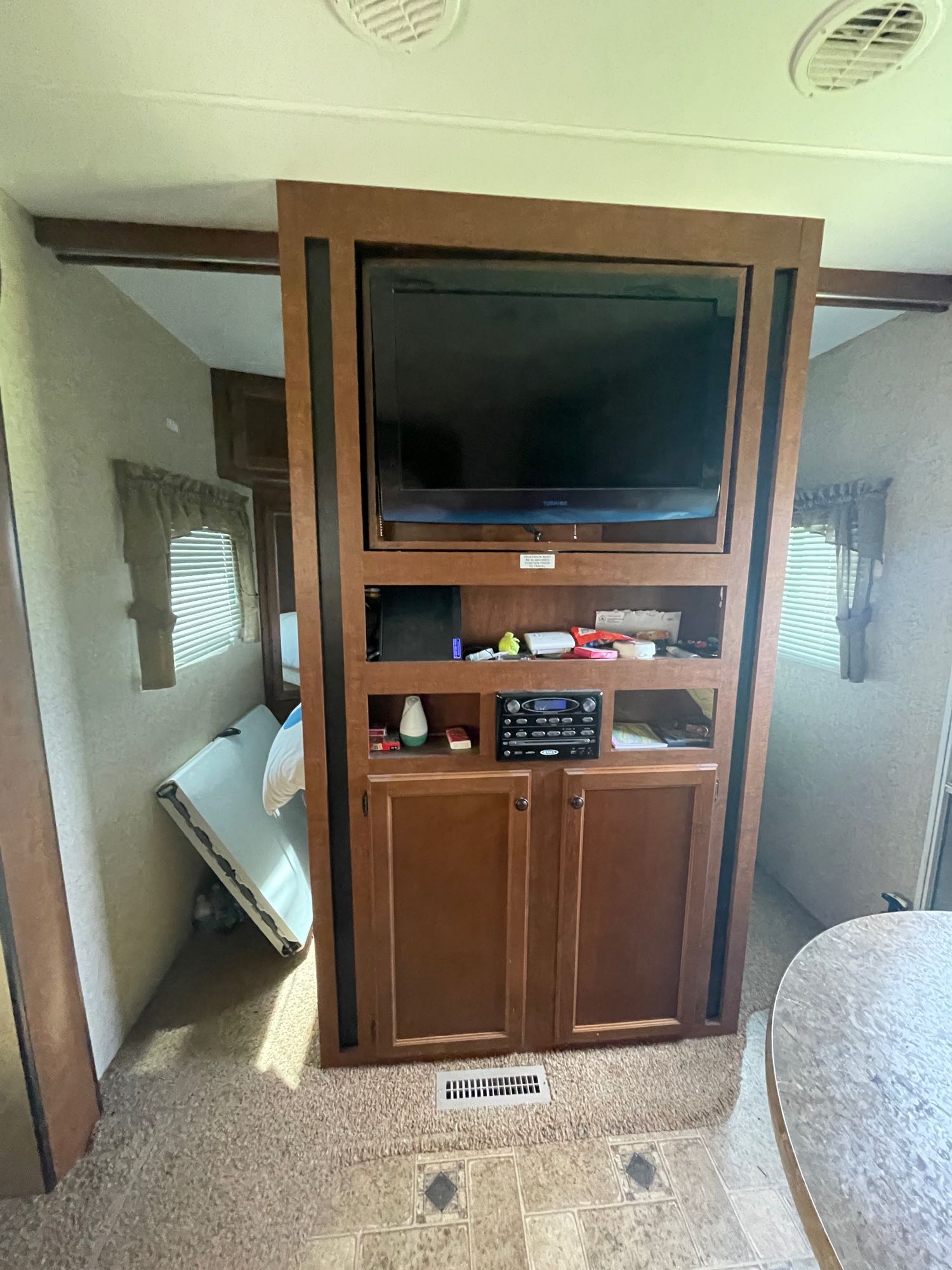 An RV rental's living area: a large wooden entertainment center with a TV and stereo, a window with blinds, and a folded bed.. Heartland Prowler 2012