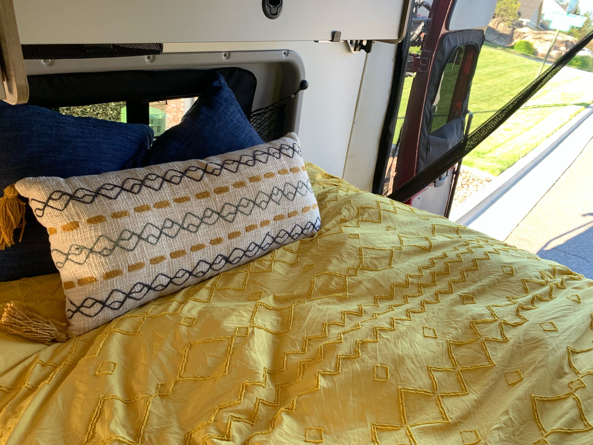 Inside a comfortable **rv rental**: yellow bedding, decorative pillows, and an open door view.. Winnebago Solis 2022