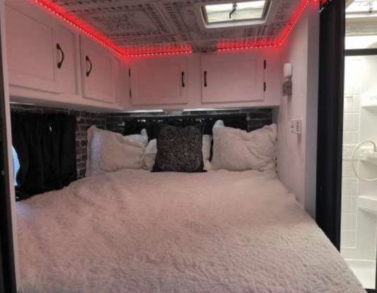 Cozy RV rental bedroom featuring a fluffy white bed, overhead cabinets with red LED lights, and a visible shower stall.. Forest River Coachmen Freelander 2010