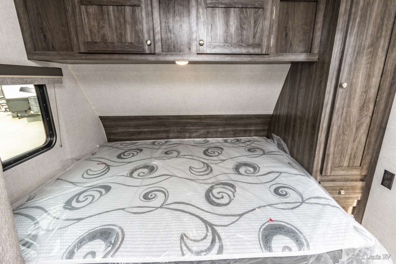 Compact RV rental bedroom with dark wood cabinets above bed, a window, and a mattress still in plastic wrap. Perfect for travel.. Highland Ridge RV Open Range 2020
